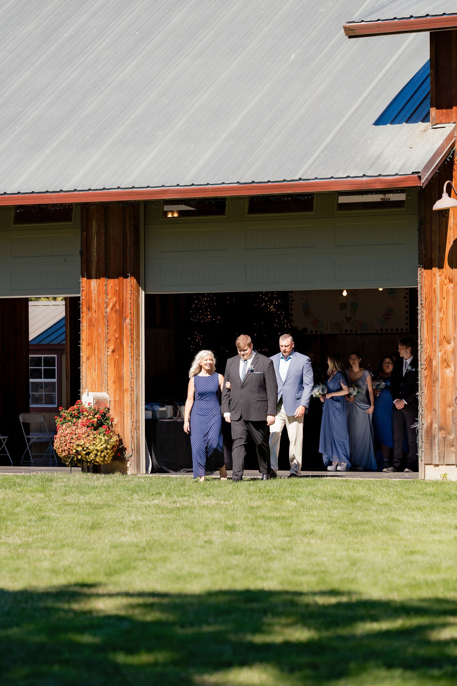 Wedding guests exit rustic barn venue in formal attire during outdoor countryside reception.