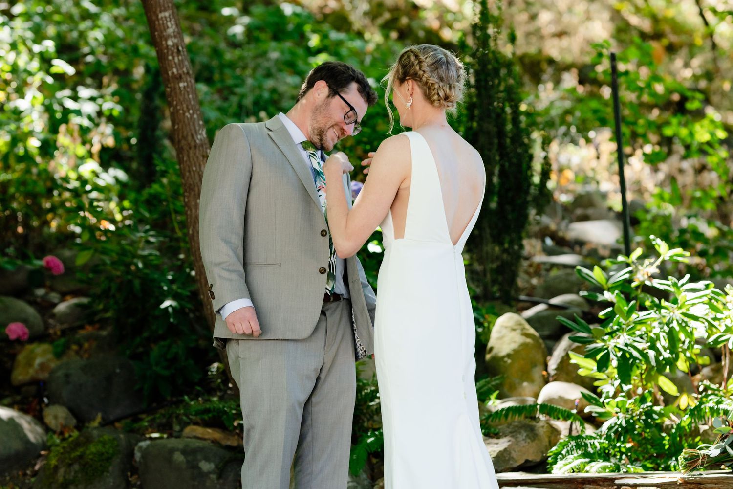 Bride and groom share an intimate moment outdoors during wedding ceremony surrounded by lush green garden foliage.