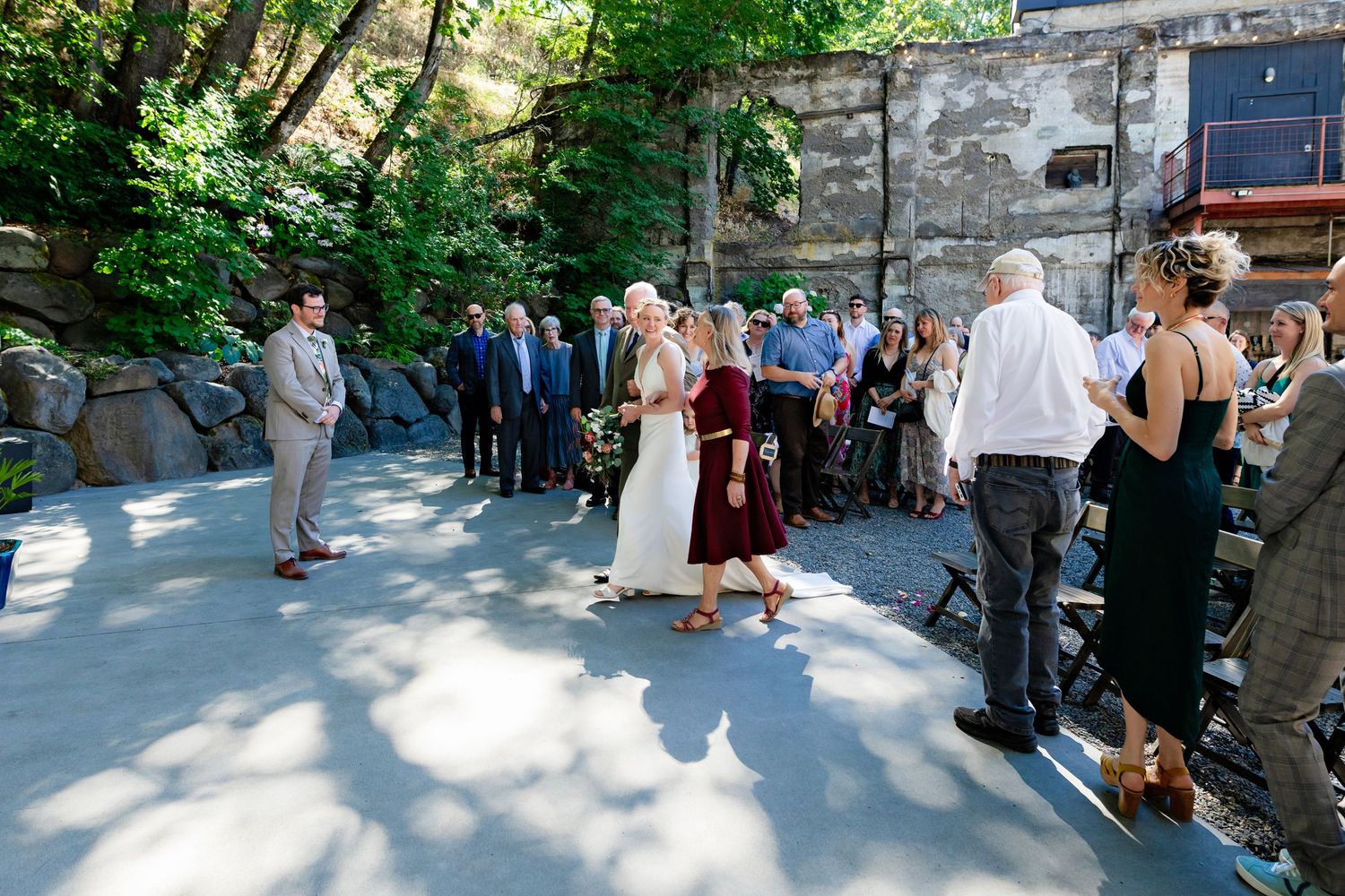 Bride walking with escort through an outdoor stone courtyard wedding ceremony surrounded by guests.