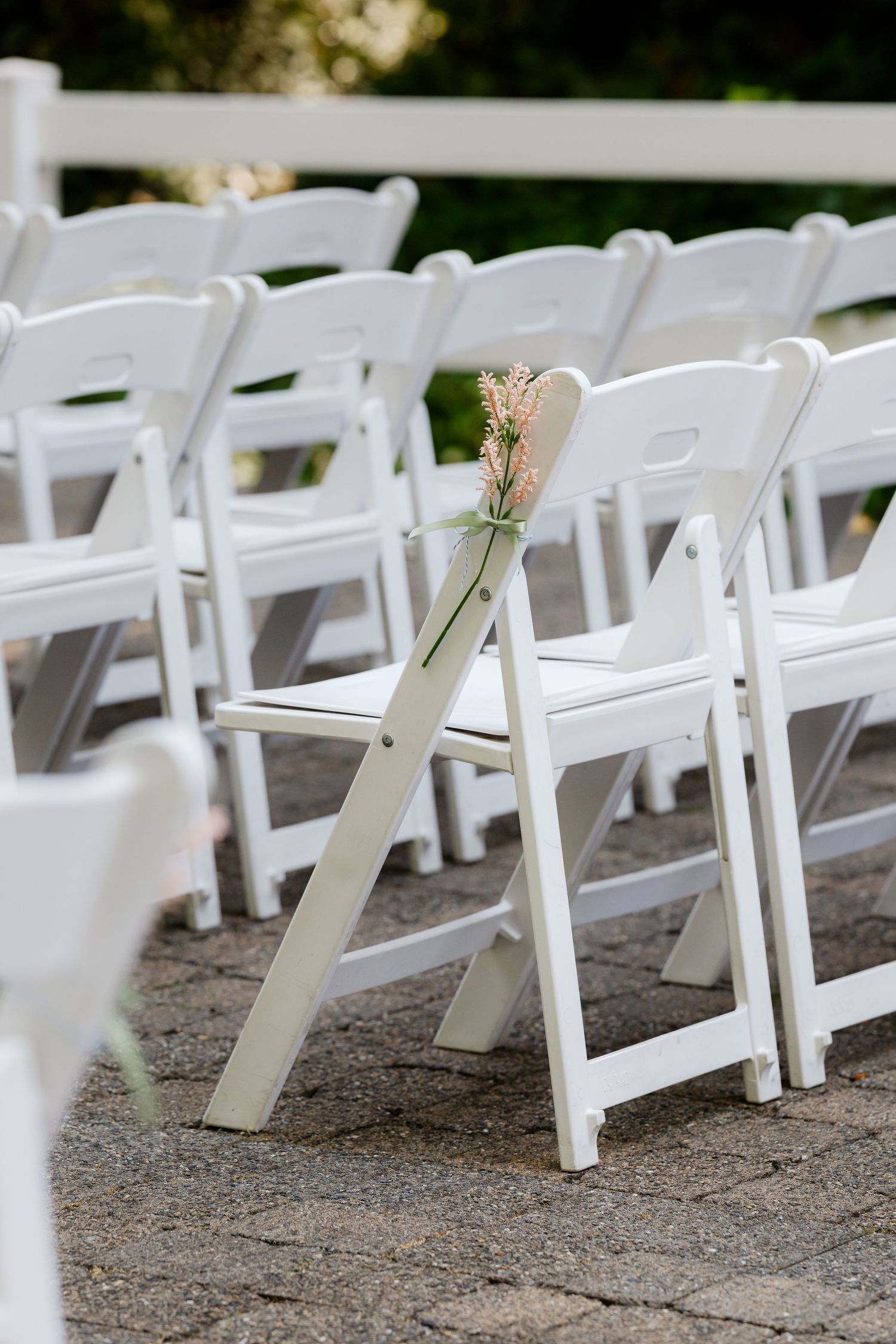 White folding chairs with floral decorations set up for an outdoor wedding ceremony.