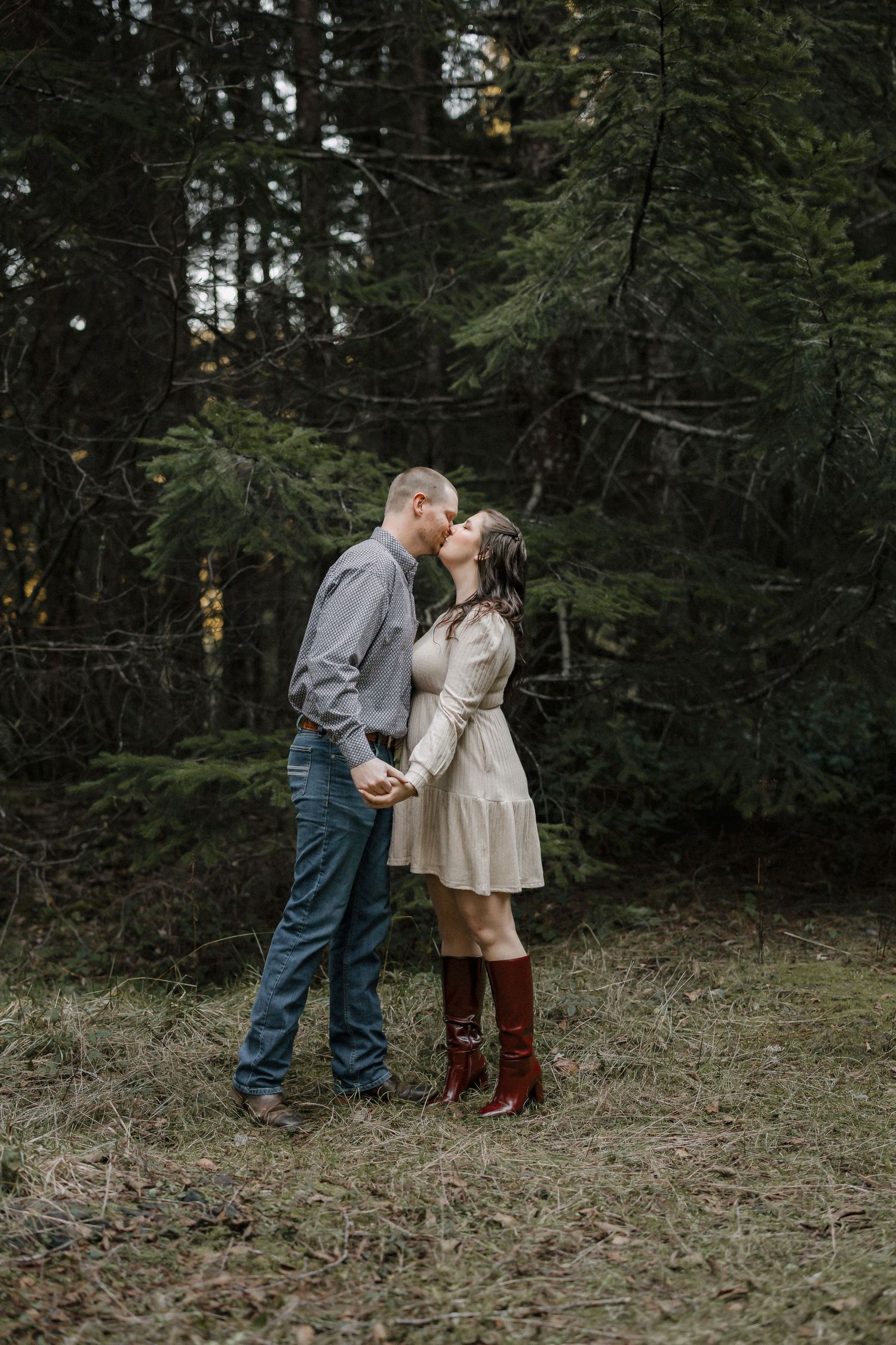 A romantic outdoor photoshoot in a moody forest setting with evergreen trees in the background.
