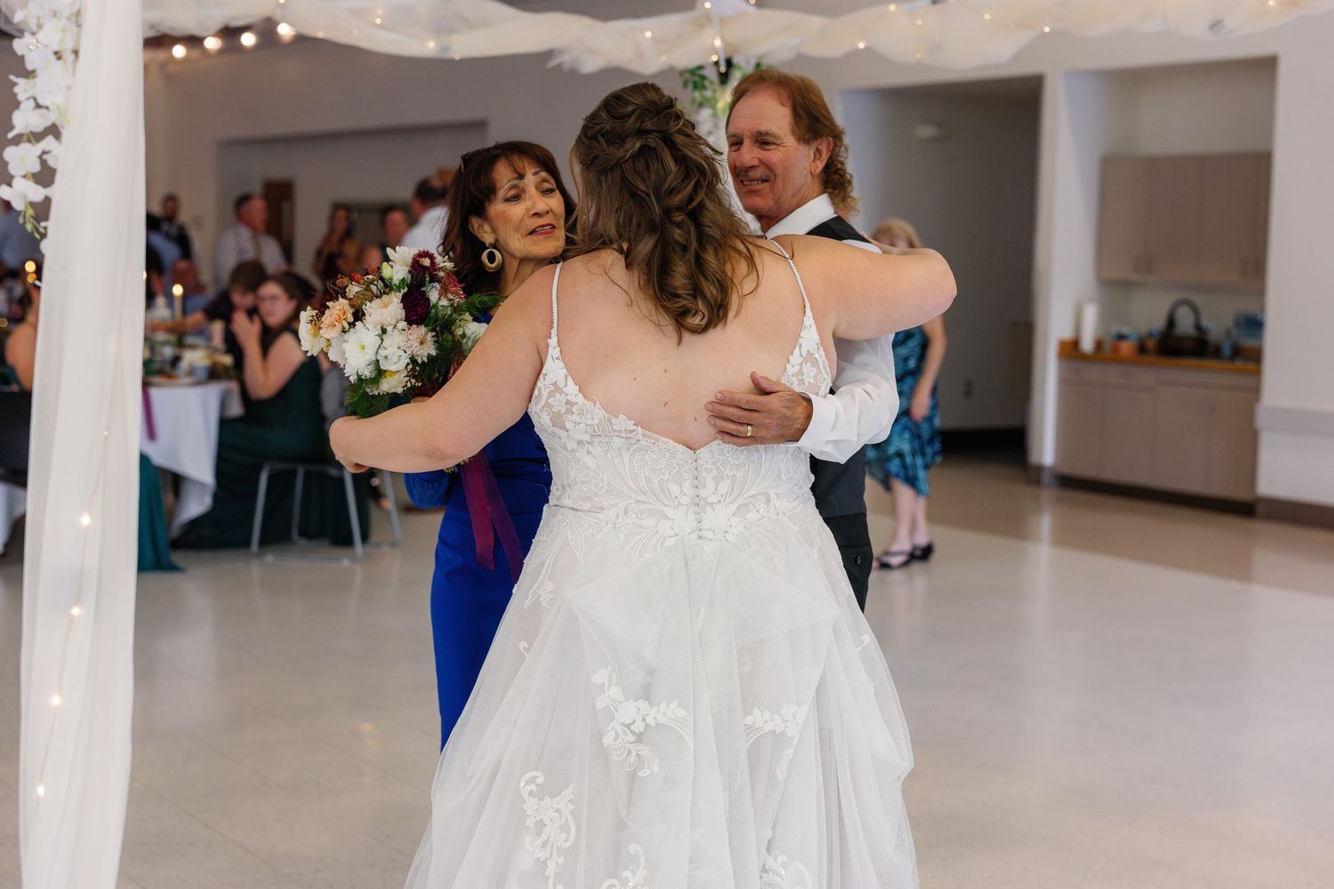 Wedding couple embracing during first dance at reception with string lights overhead.