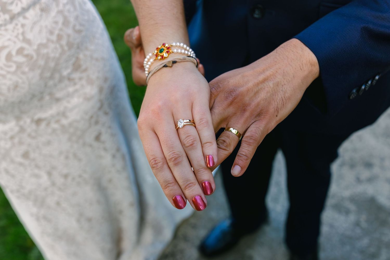 Close-up details of wedding rings and hands against formal wedding attire.