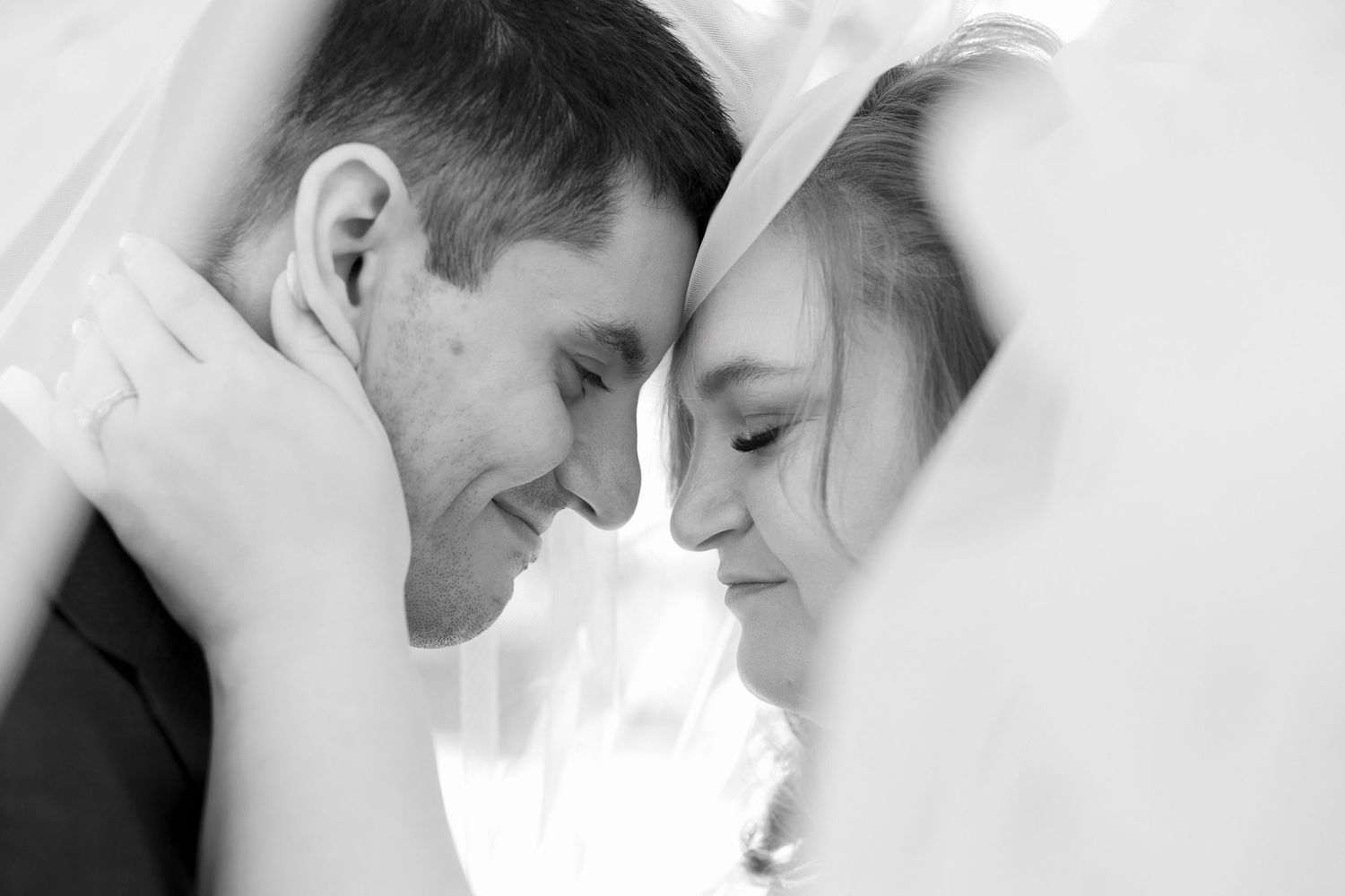 Intimate black and white close-up portrait of a couple in wedding attire sharing a tender moment.