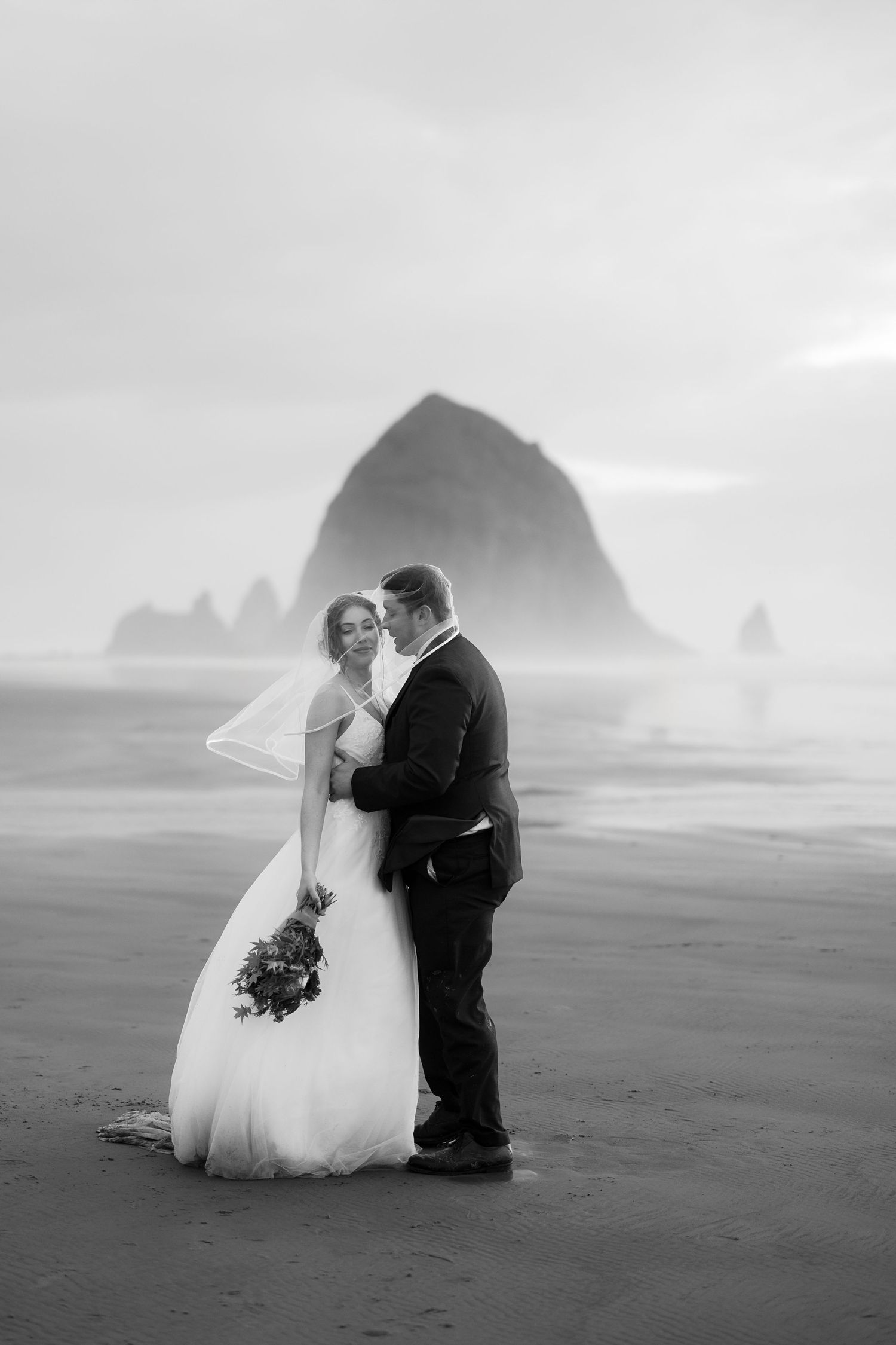 A dreamy beach wedding photo with Haystack Rock creating a dramatic backdrop in the mist.