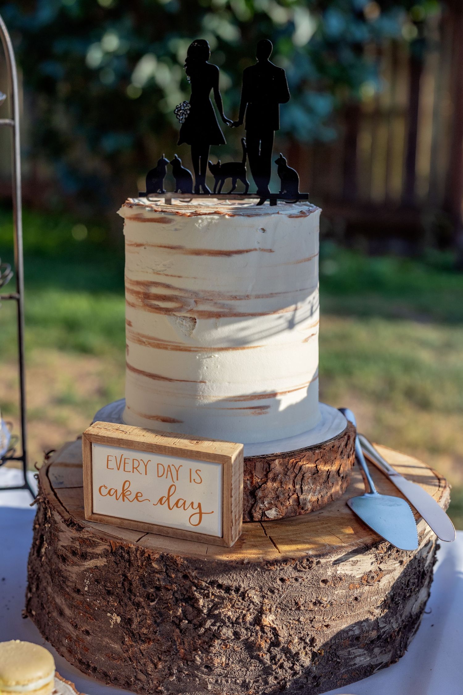 Rustic wedding cake with silhouette topper displayed on wood slice stands with 'Every Day is Cake Day' sign.