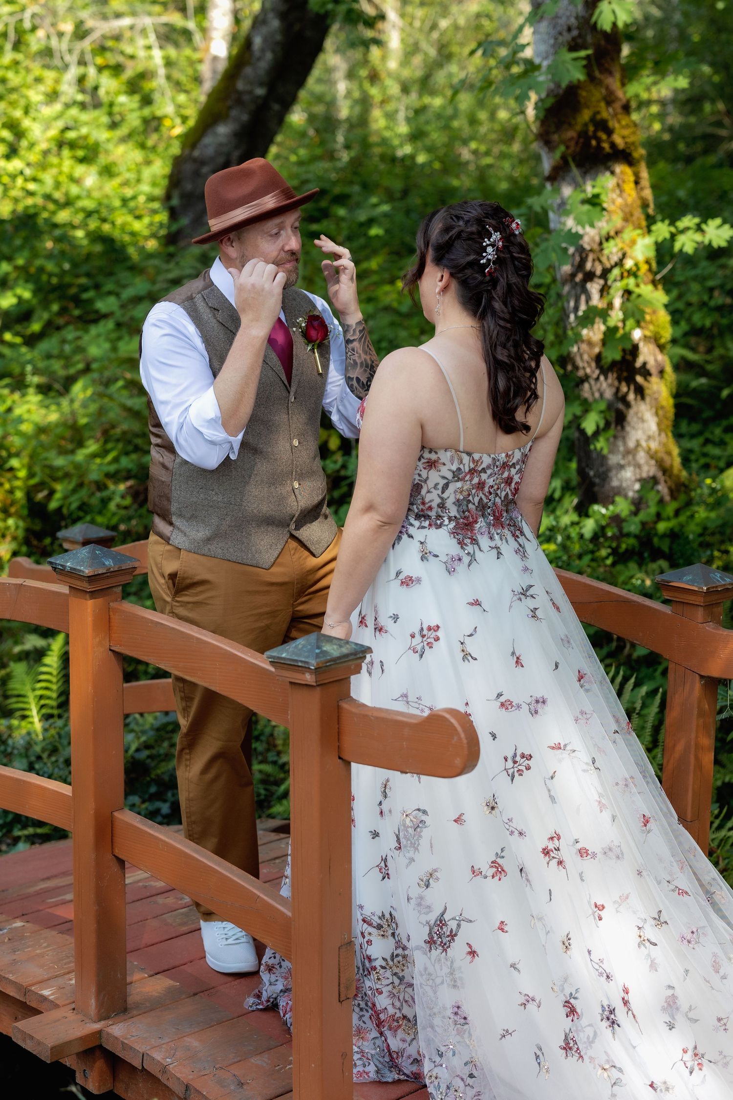 Couple sits together on wooden bench in garden during wedding photoshoot.