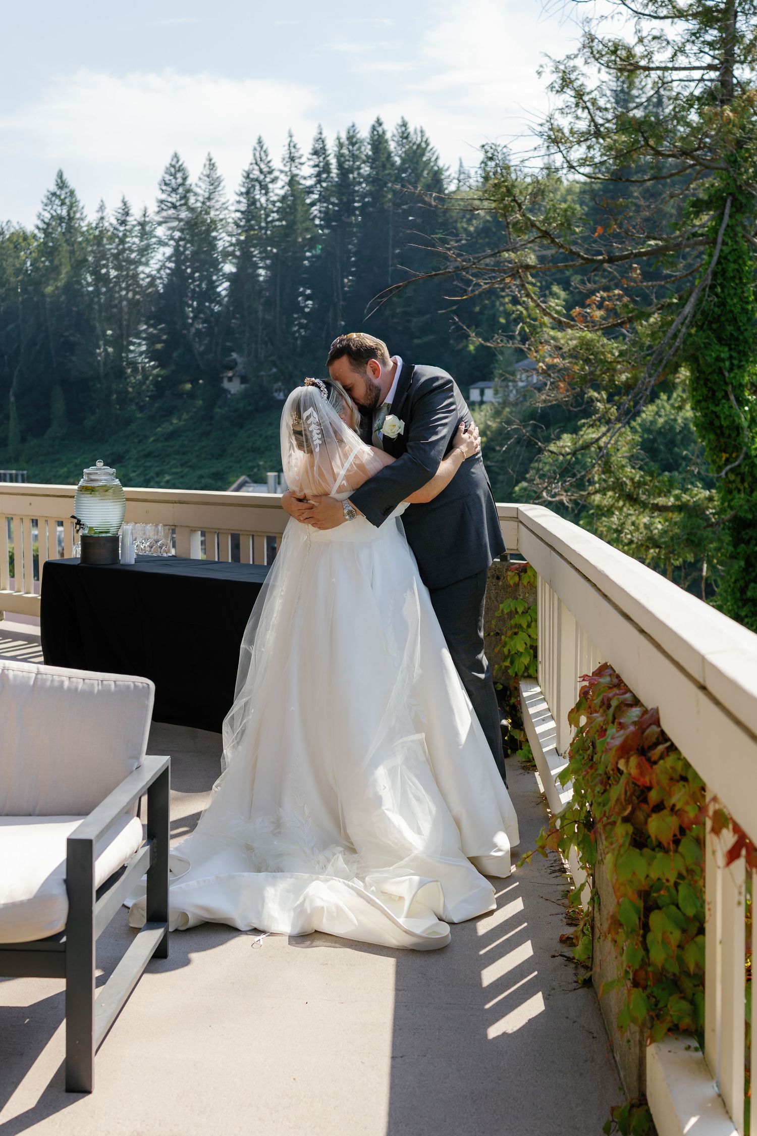 Wedding couple sharing an intimate moment on an outdoor deck surrounded by evergreen trees.