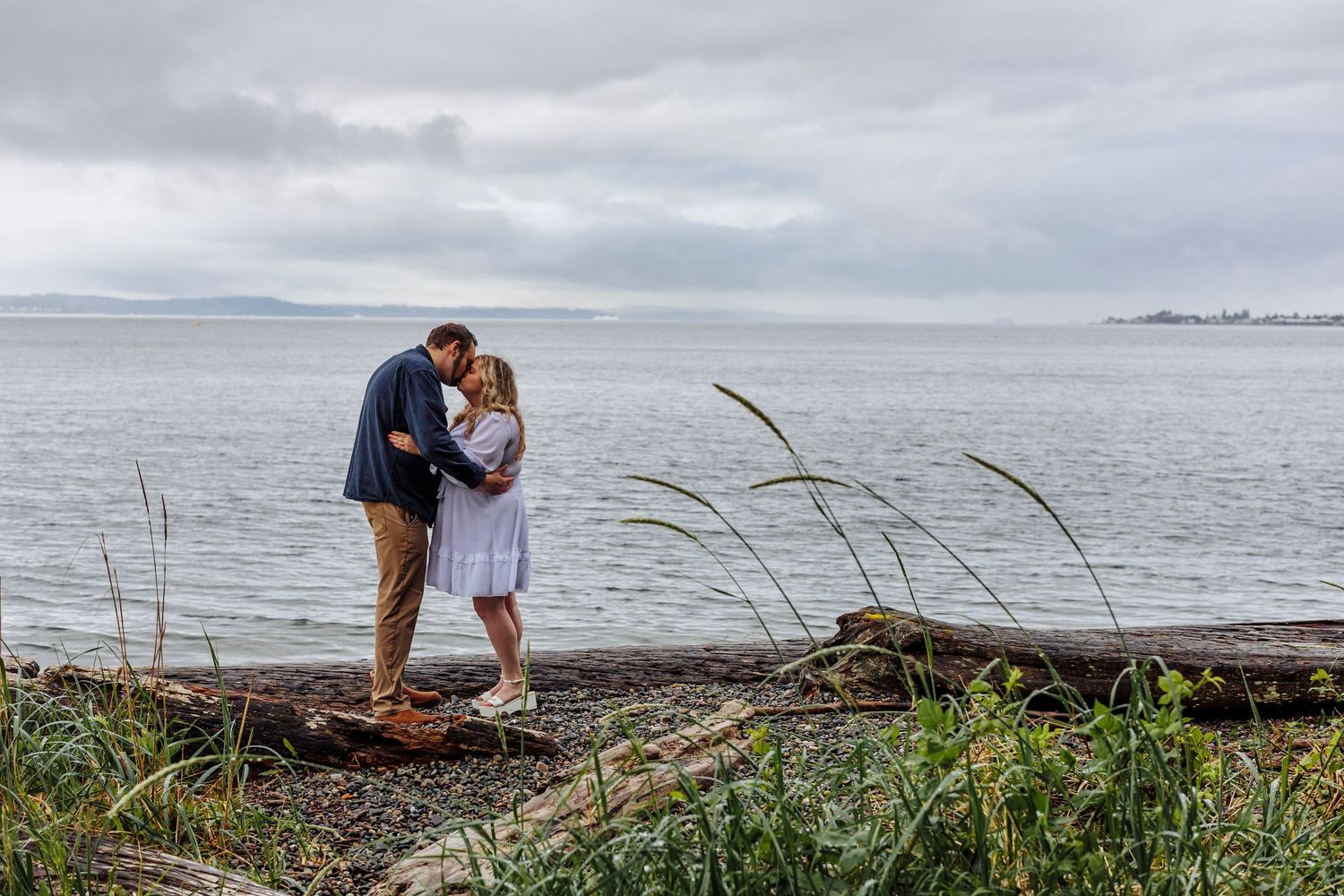 A romantic moment shared on a rocky coastal shoreline under moody cloudy skies.