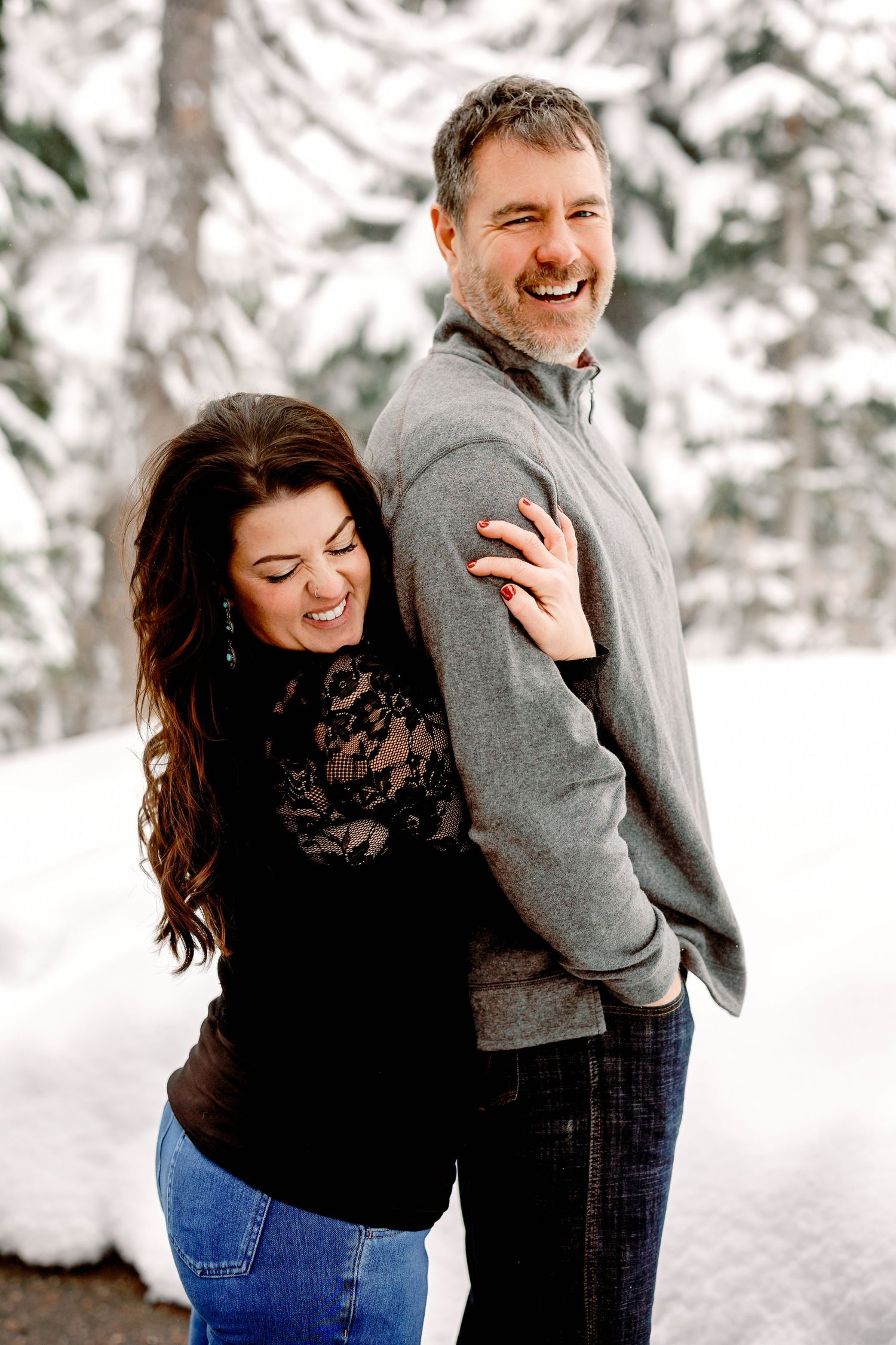 A couple shares joyful laughter together during a winter photo session in the snow.