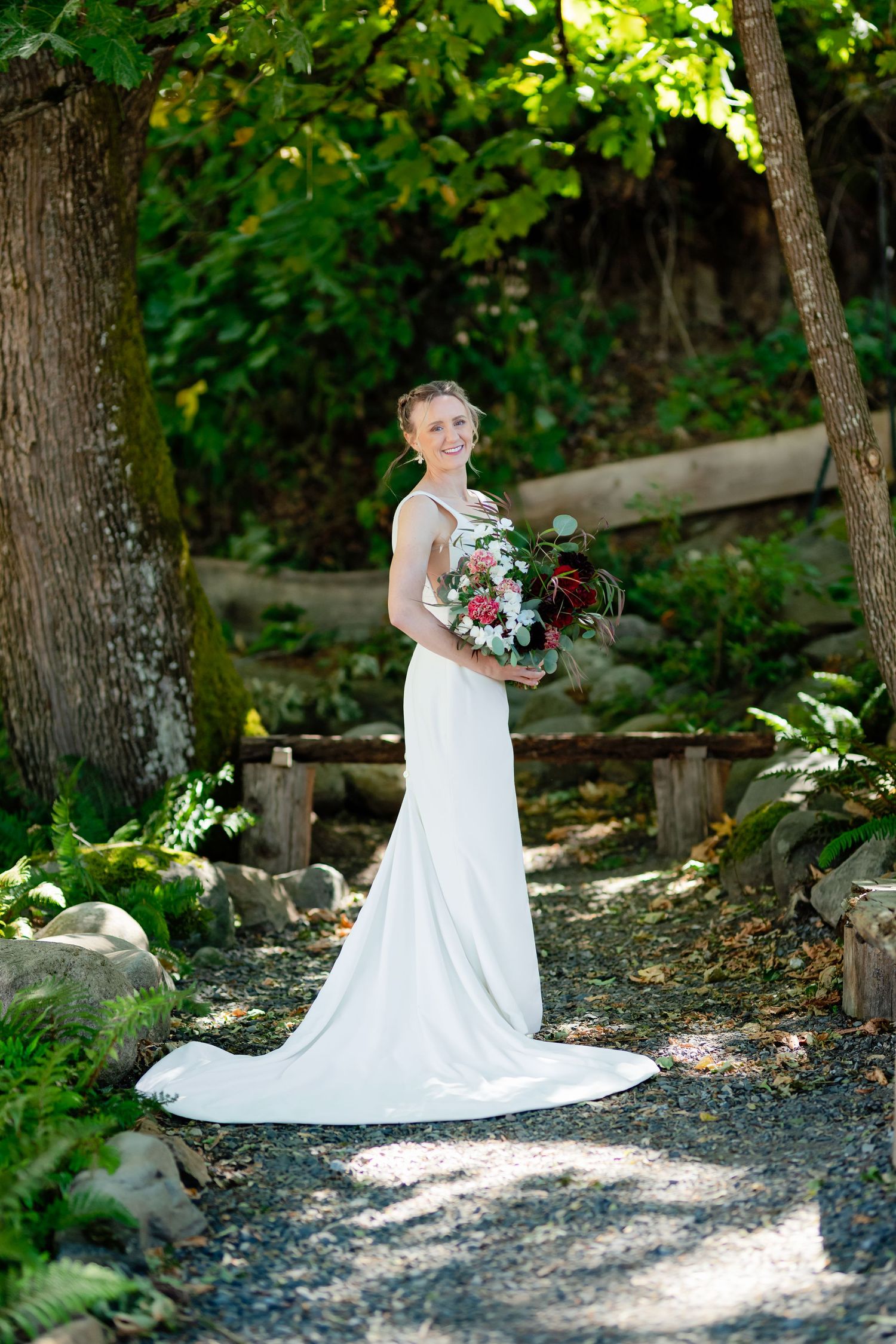 Bride in white gown holding bouquet on garden path.
