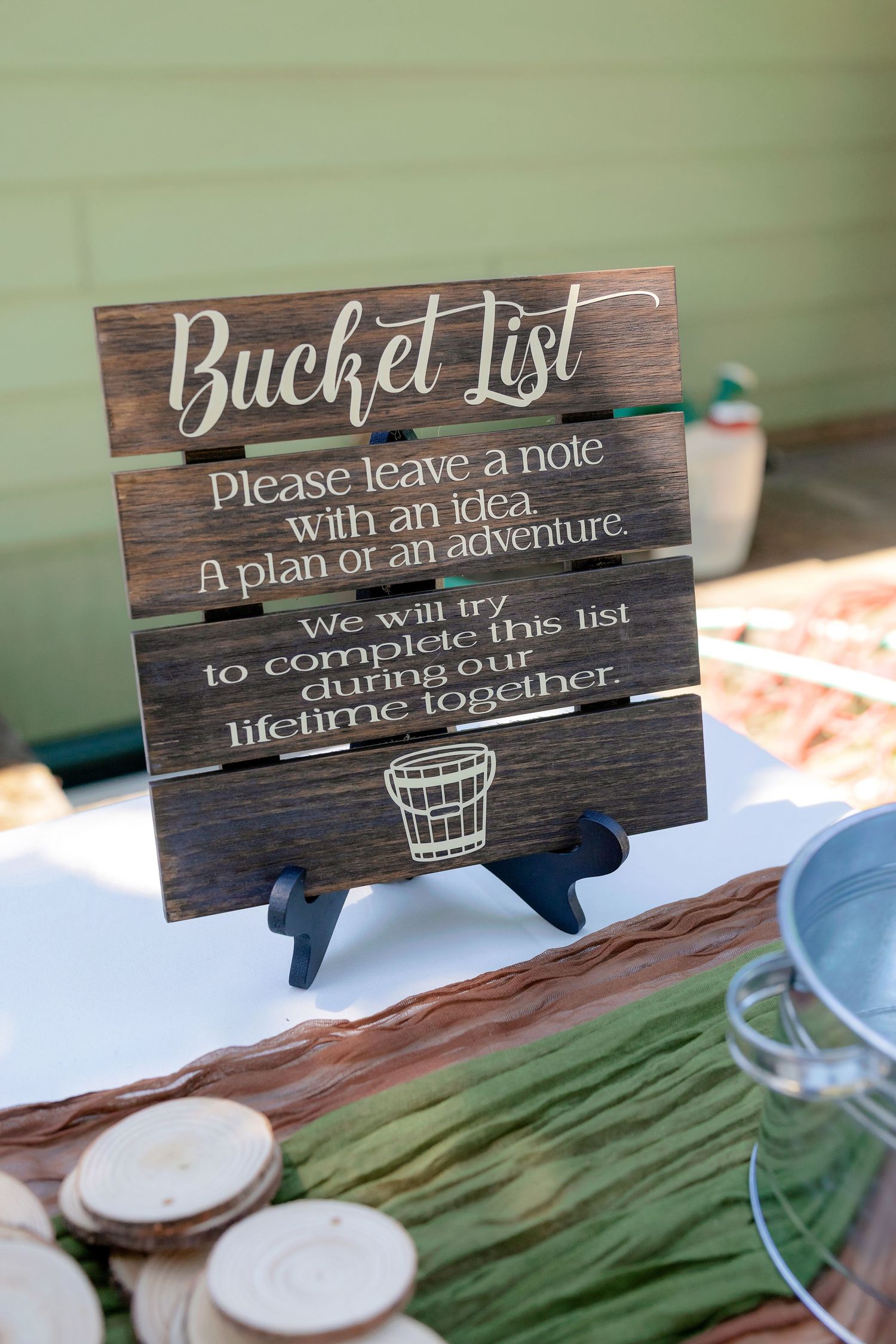 Rustic wooden Bucket List wedding sign asking guests to leave ideas for adventures the couple will complete together.