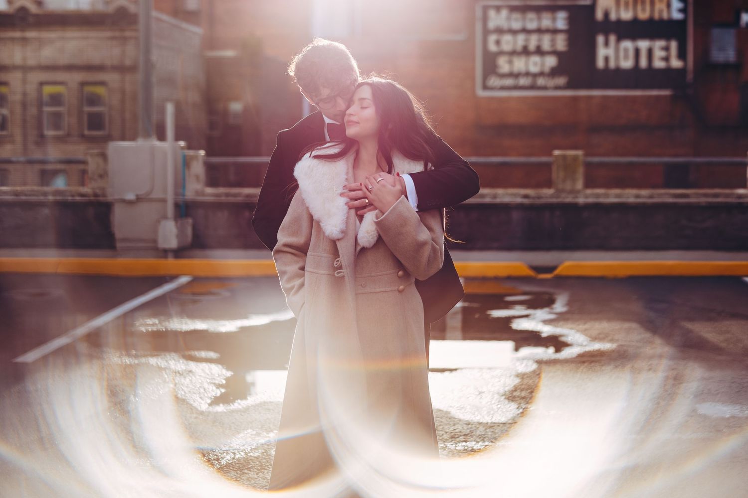 Couple sharing intimate moment in moody urban setting with warm backlit glow at dusk.