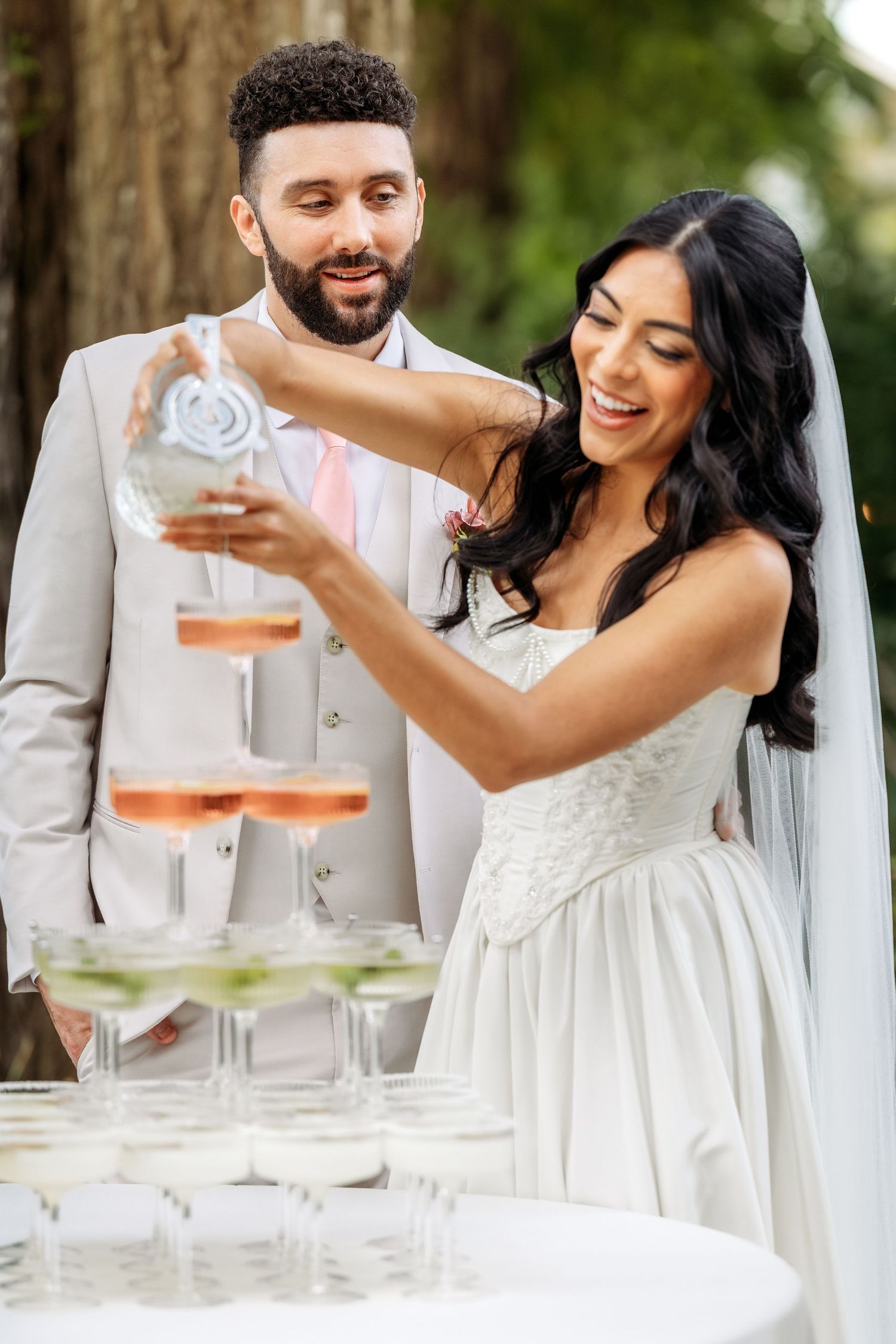 Newlyweds share a joyful moment while pouring champagne at their outdoor wedding reception.
