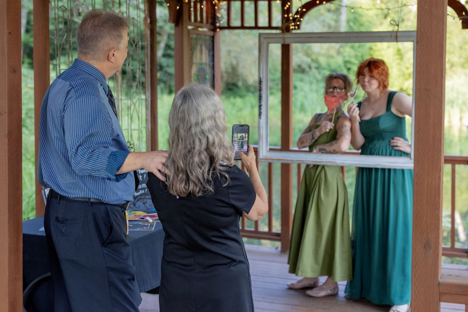 Wedding party gathers in a rustic wooden gazebo surrounded by green foliage during an outdoor celebration.