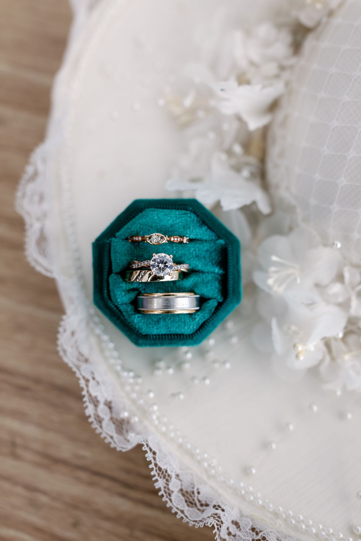 Wedding rings displayed on emerald green velvet ring boxes with delicate white lace accents.