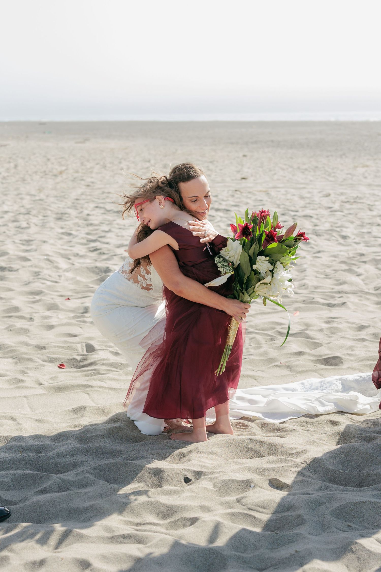 Emotional beach scene with embraces and floral bouquets on sandy shores.