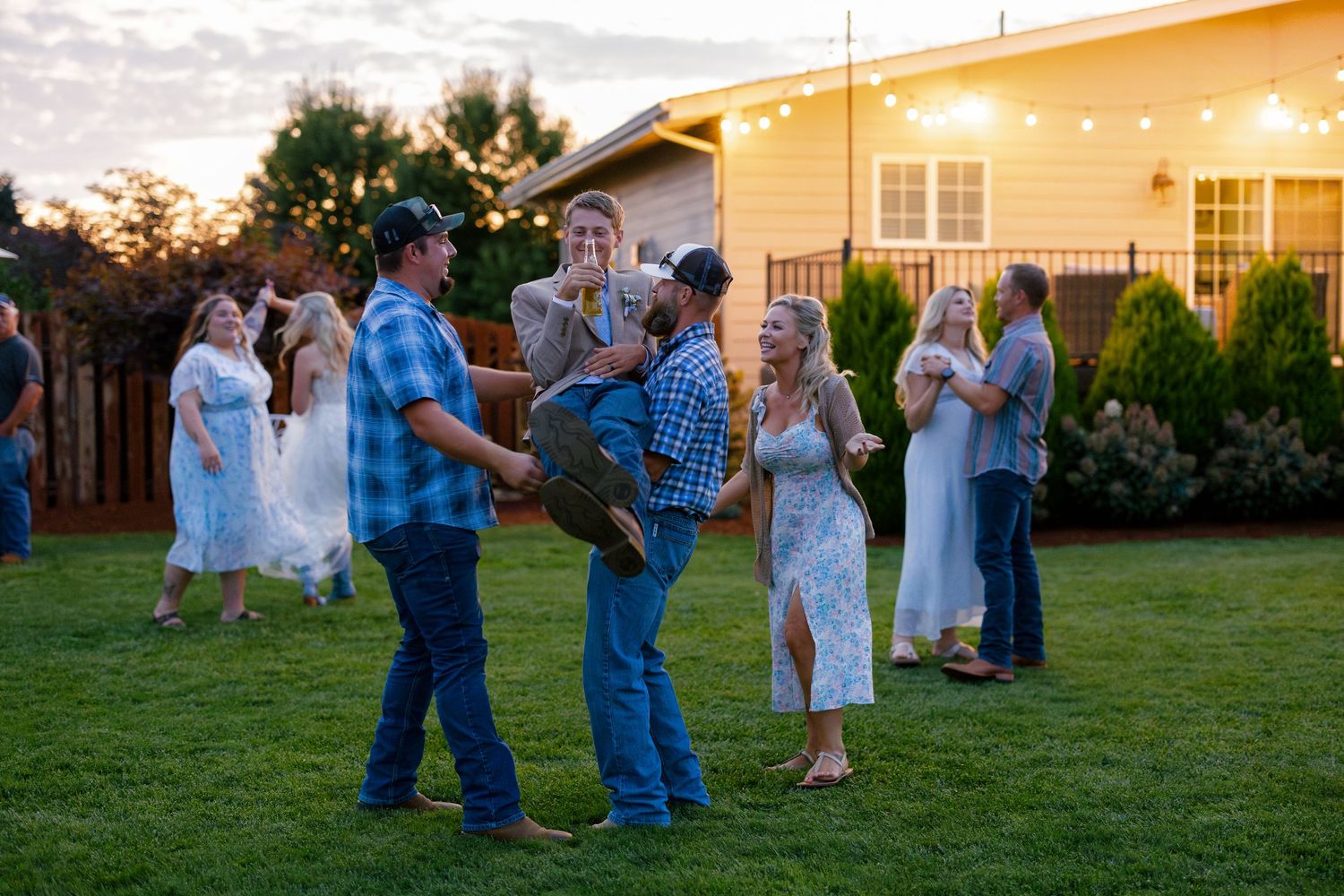 Couples dancing together on a grassy lawn at sunset during an outdoor celebration event.