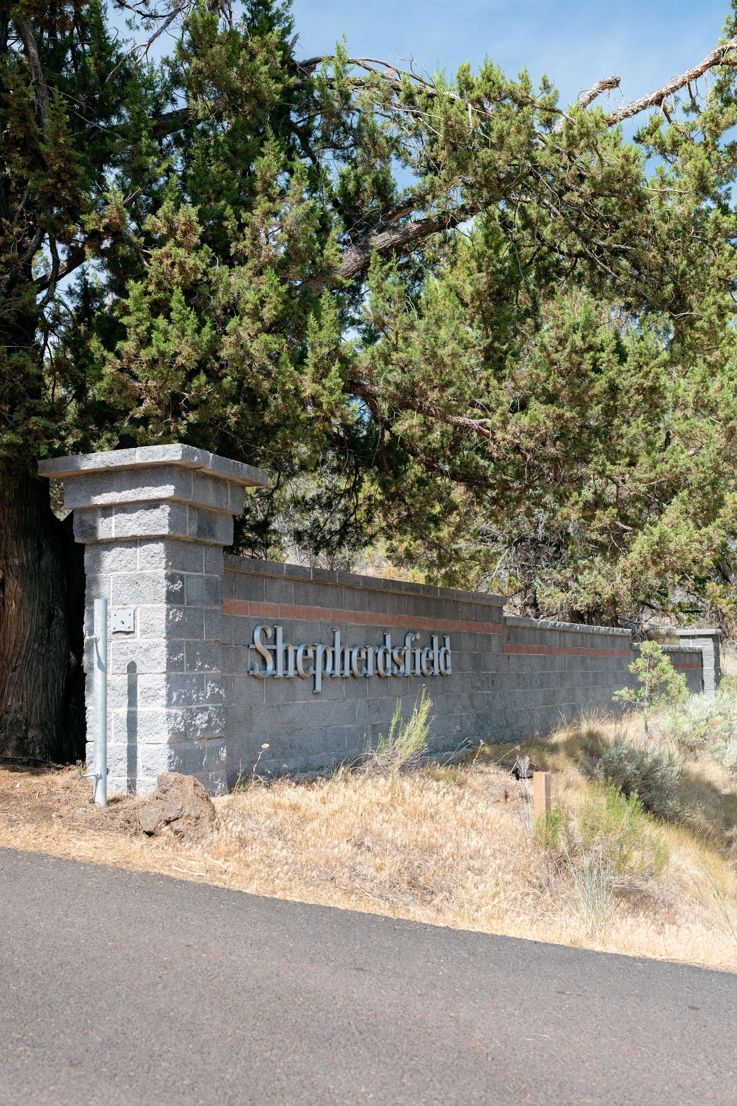 Stone entrance sign reading Shepherdsfield surrounded by pine trees on a sunny day.