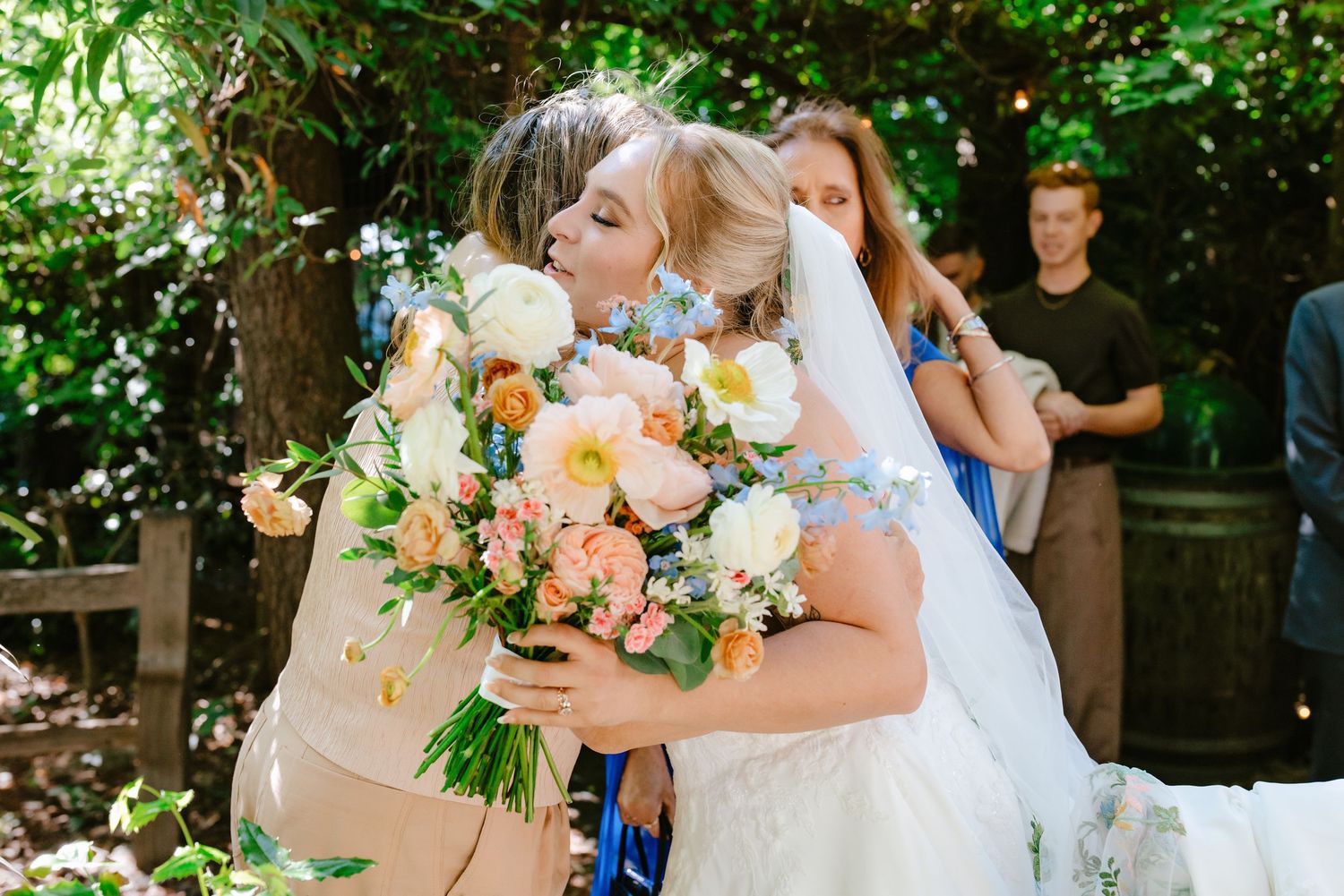 Bride in white wedding gown hugs guest while holding peach and white bridal bouquet.