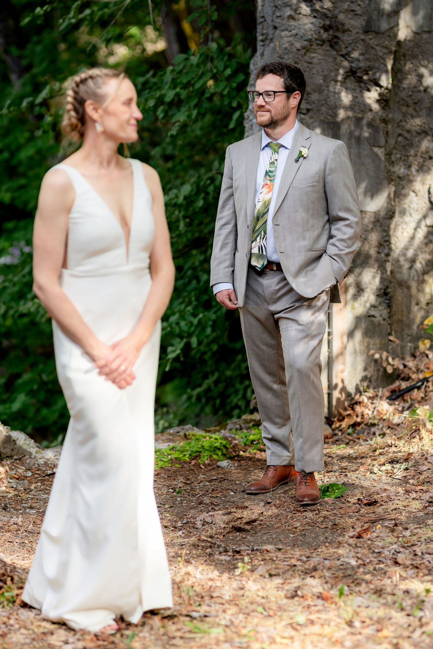 Groom in gray suit with floral tie gazes at bride in white gown during outdoor wedding first look.