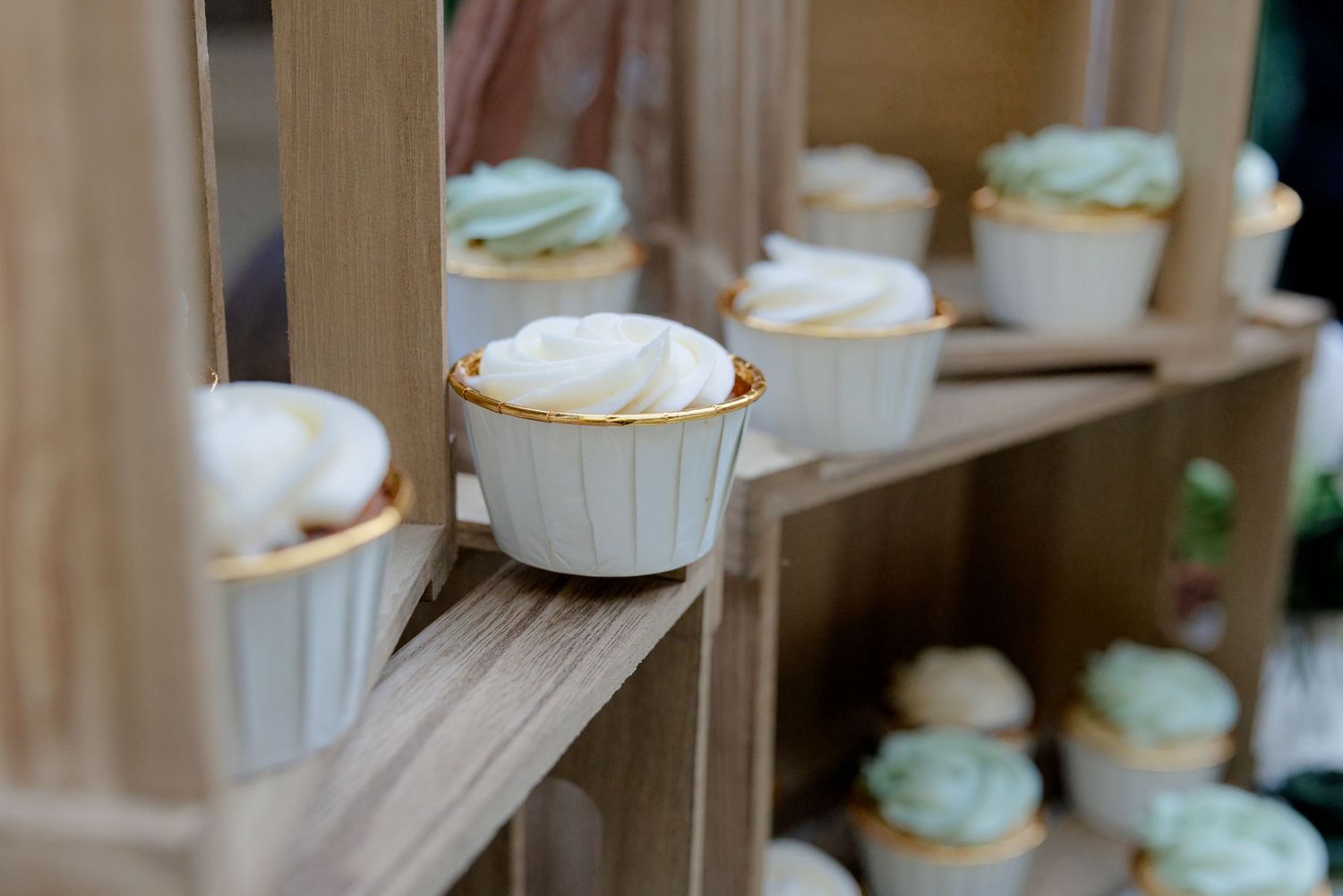 Close-up of elegant white and gold cupcakes displayed on rustic wooden shelves.