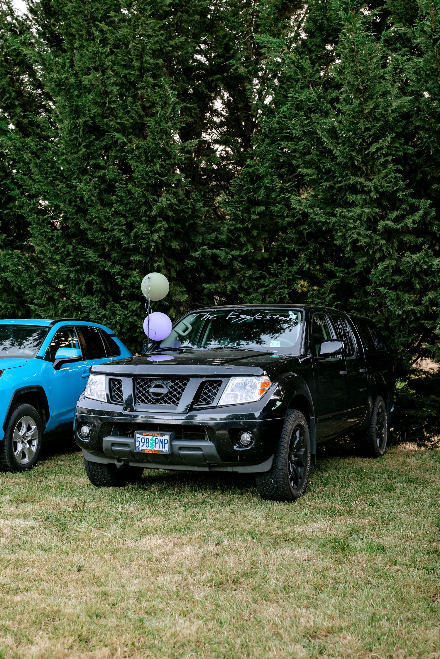 Black Nissan Frontier truck decorated with balloons parked on grass at a wedding.