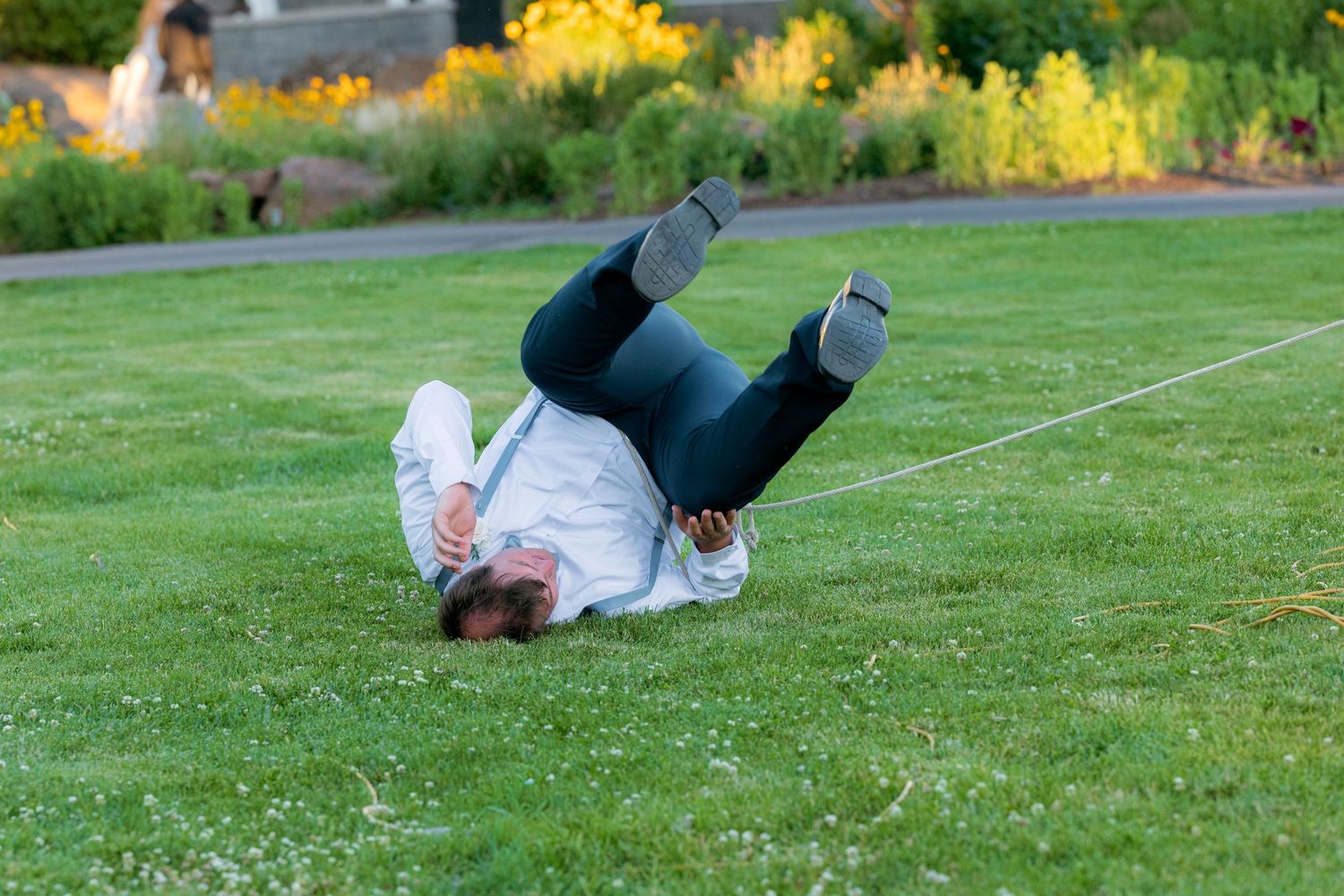Man tumbling and rolling on green grass lawn near a rope during outdoor event.
