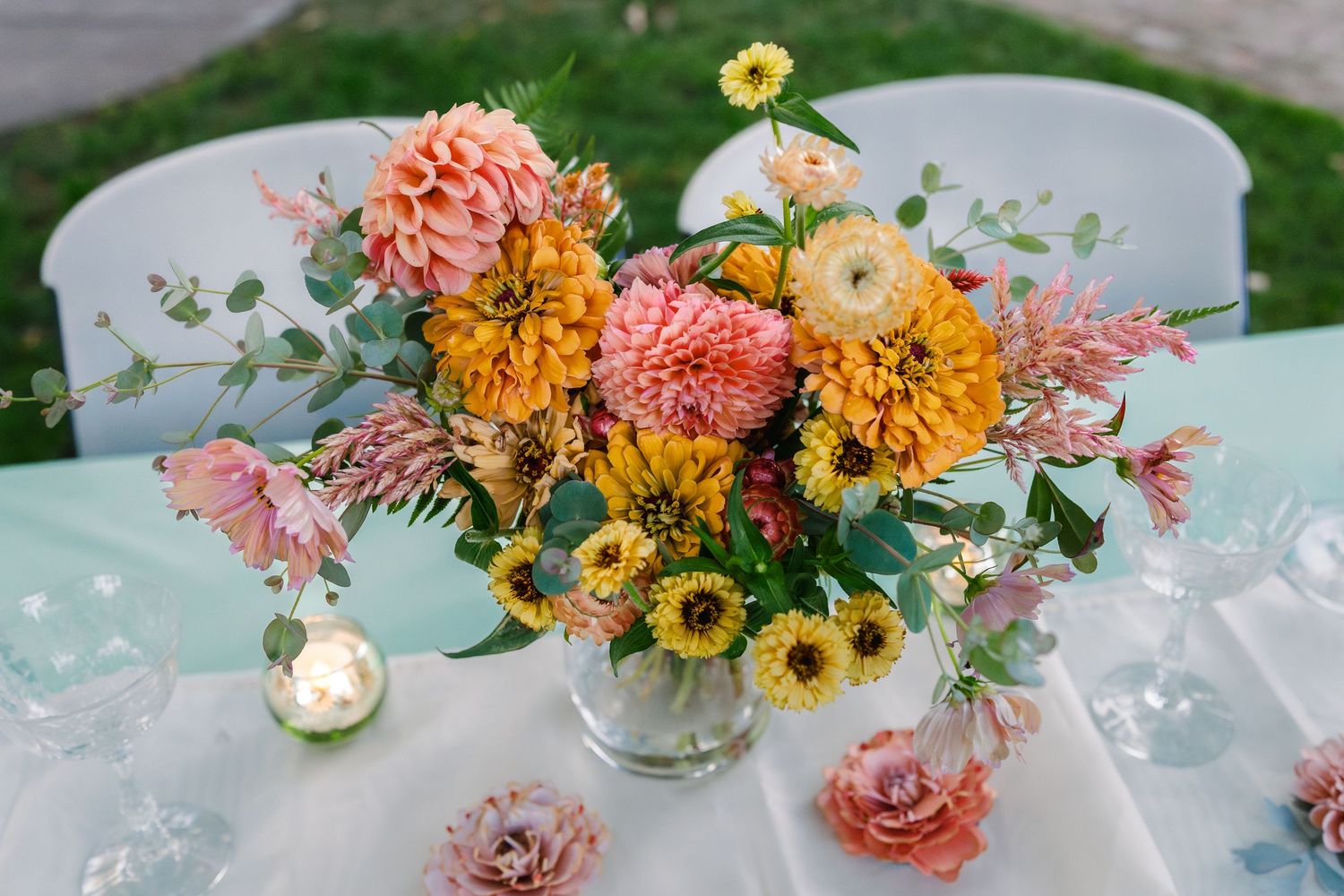 Colorful floral centerpieces with sunflowers and pink roses decorate tables at an outdoor event.