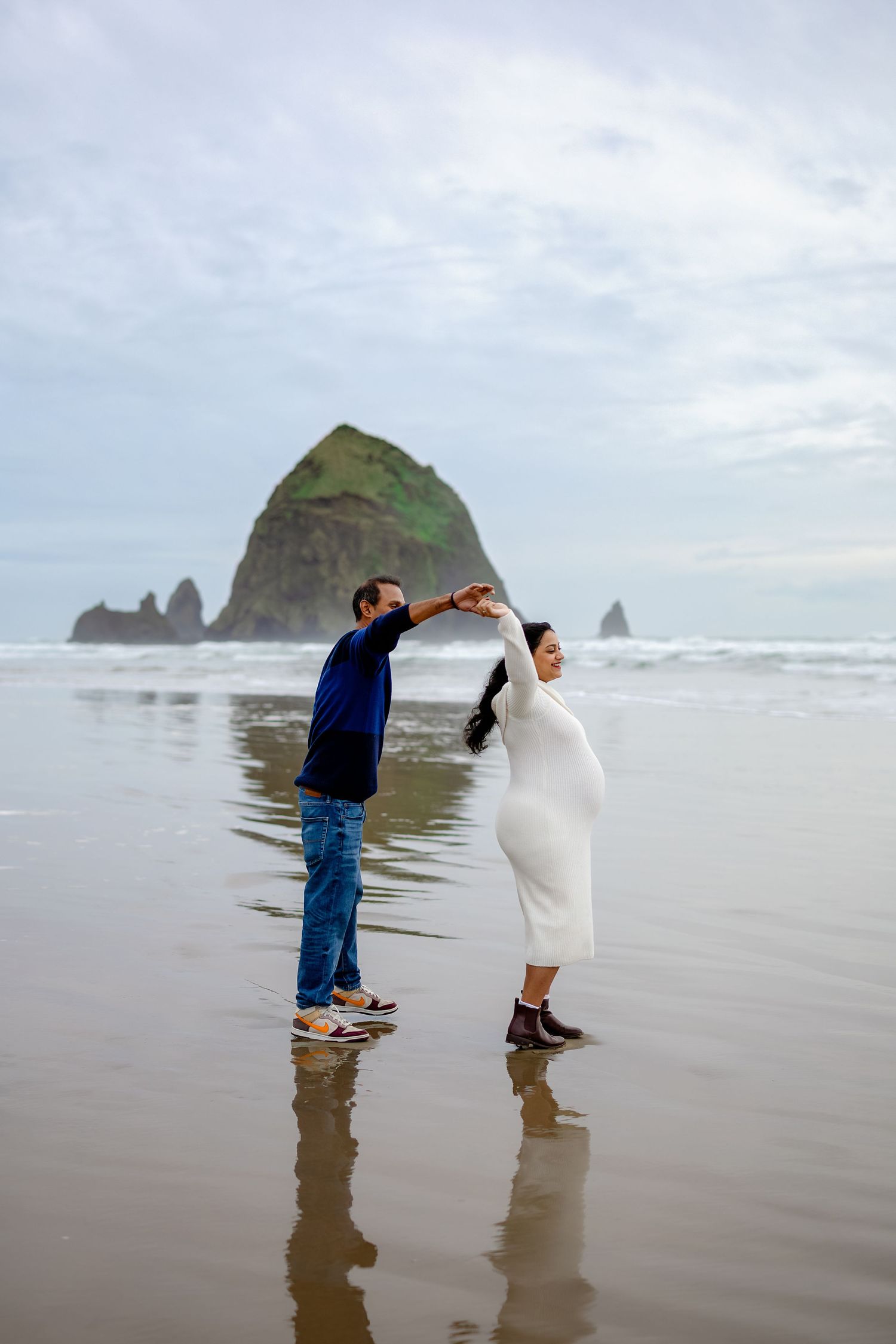 A couple plays in the shallow water at Cannon Beach with Haystack Rock visible in the distance.