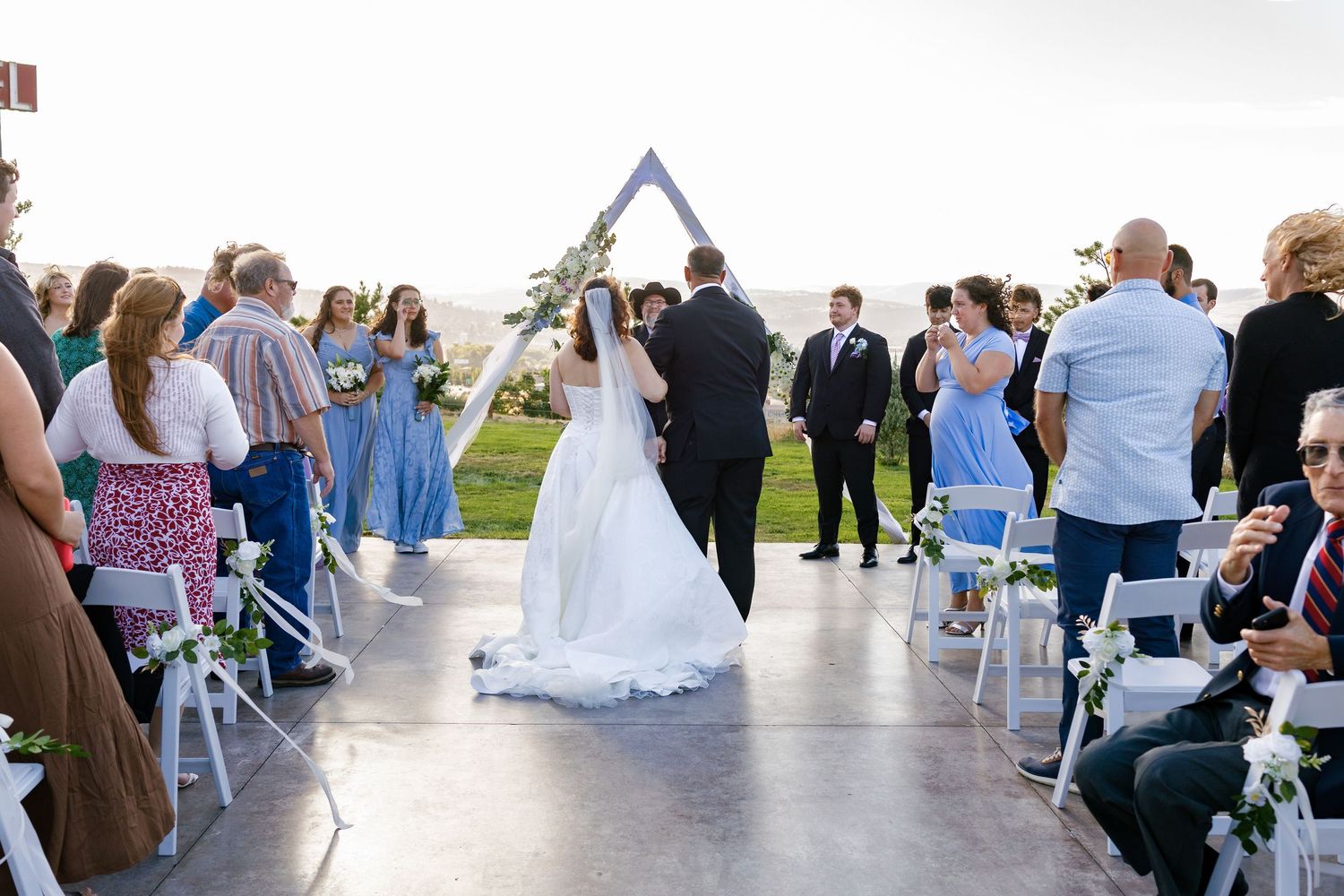 Wedding ceremony setup with white chairs and blue accents under an open sky.
