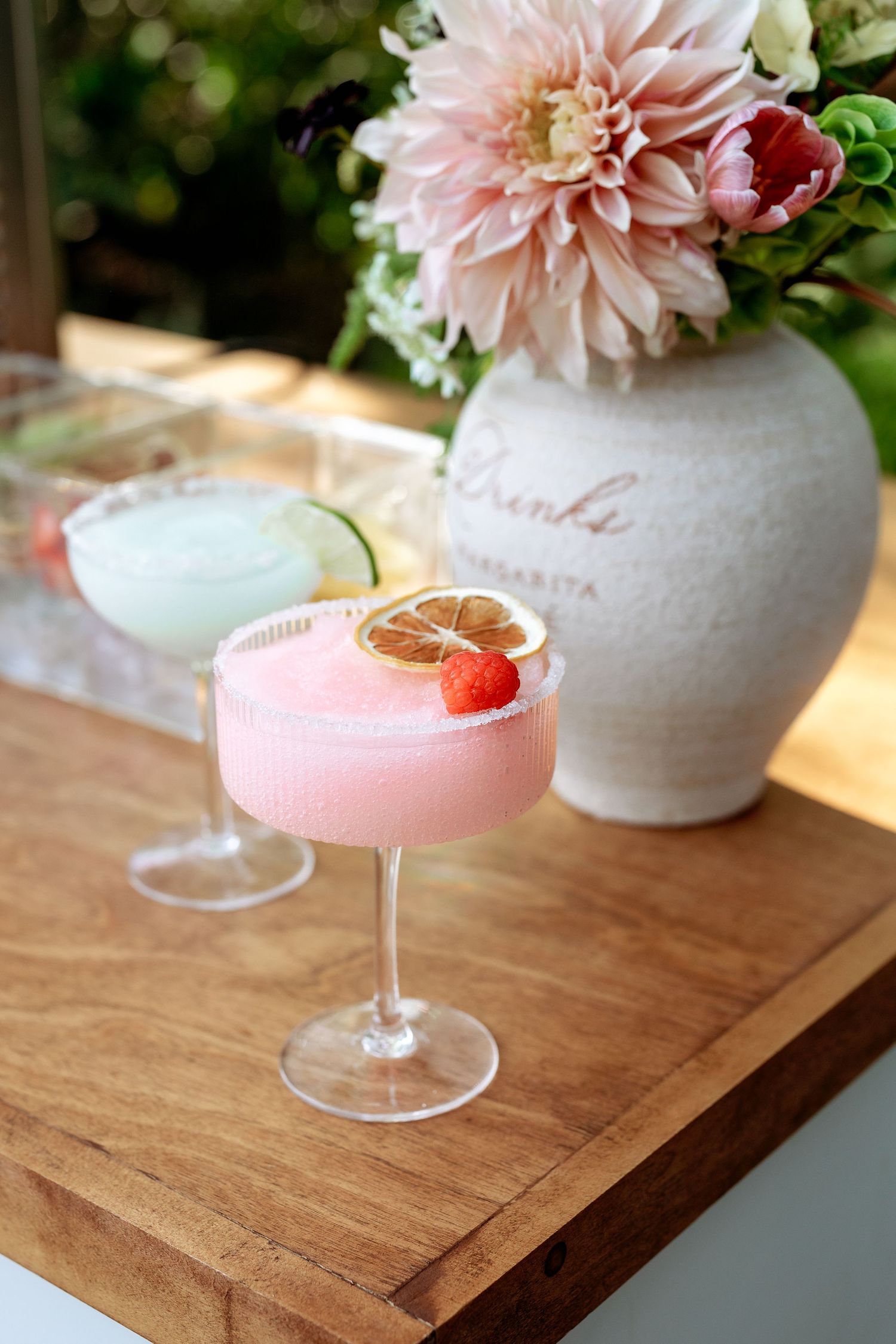 Pink cocktails garnished with raspberries served alongside blush dahlias in ceramic vases.