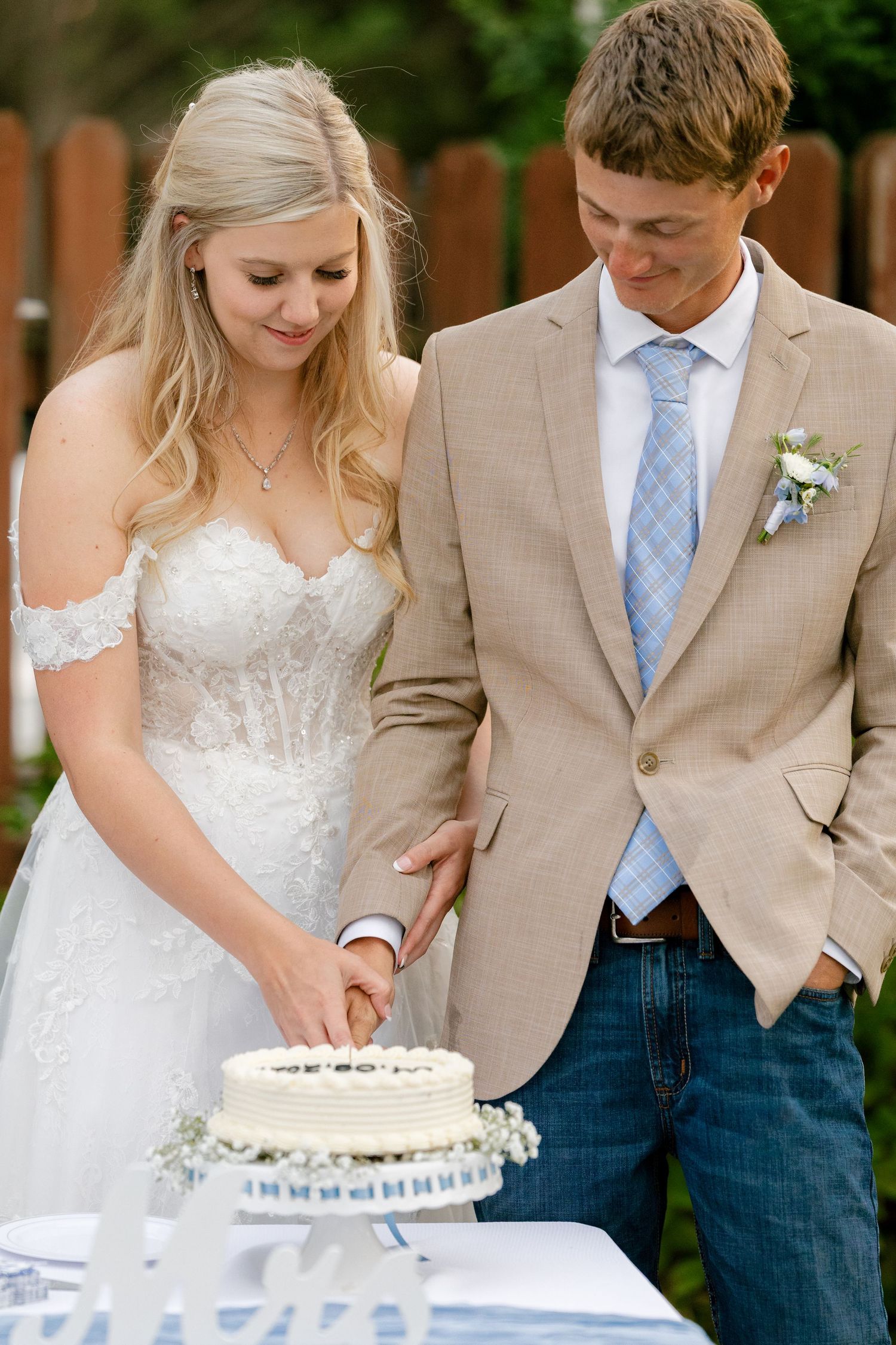 A couple cuts their wedding cake together on their special day in an outdoor garden setting.