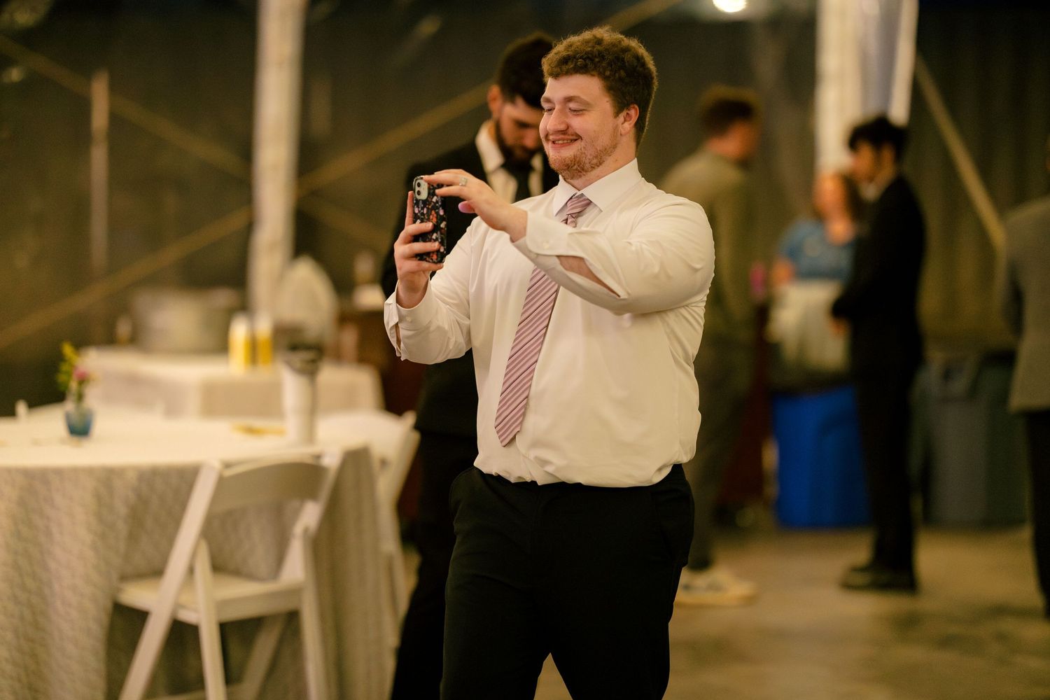 Wedding guests using smartphones and cameras to capture moments during an indoor reception.