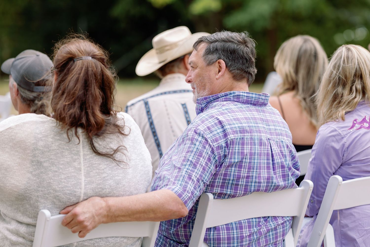 A group of people dance together outdoors wearing coordinated purple and white plaid shirts.