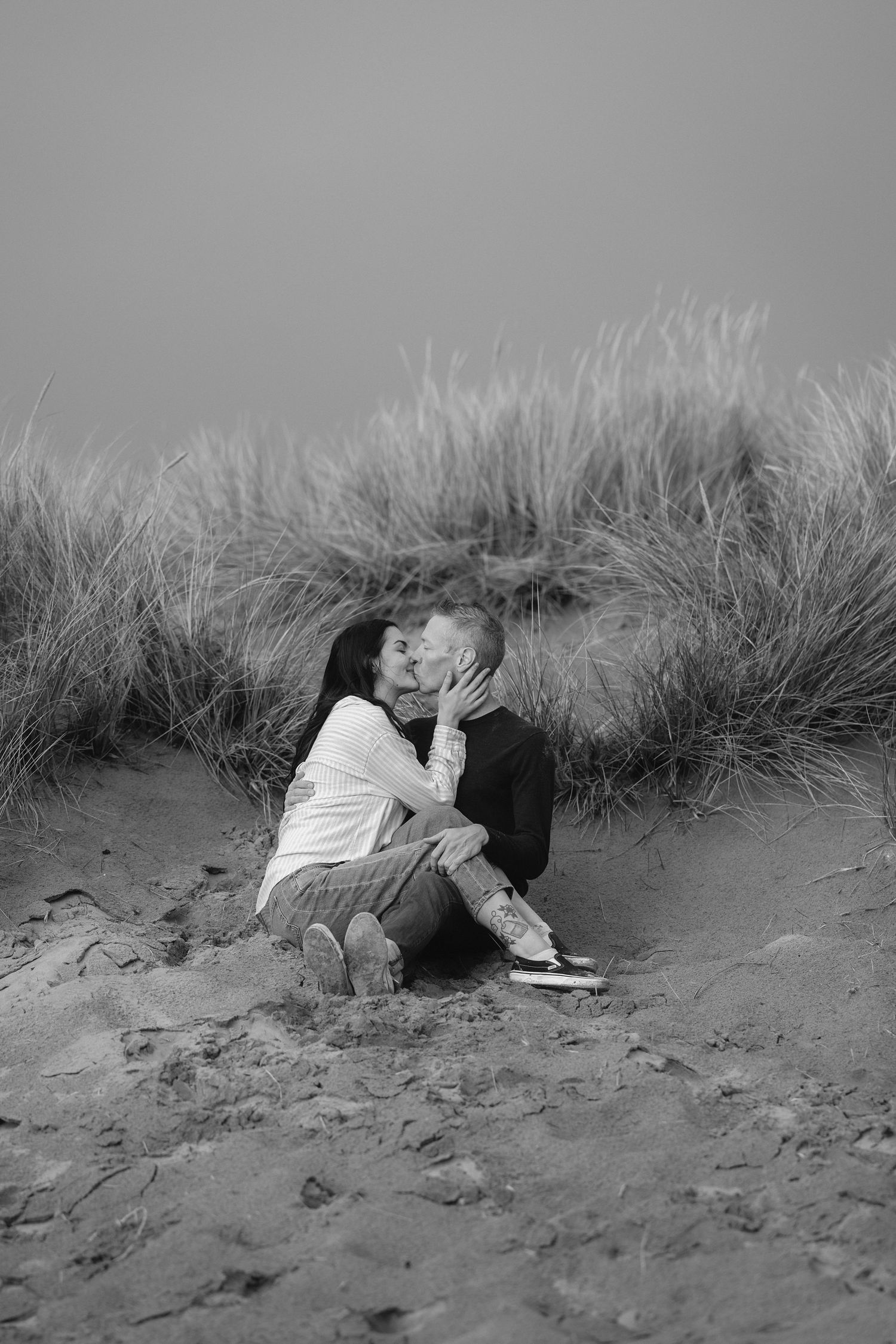 Black and white photo series showing two people lying together in beach grass and sand dunes.