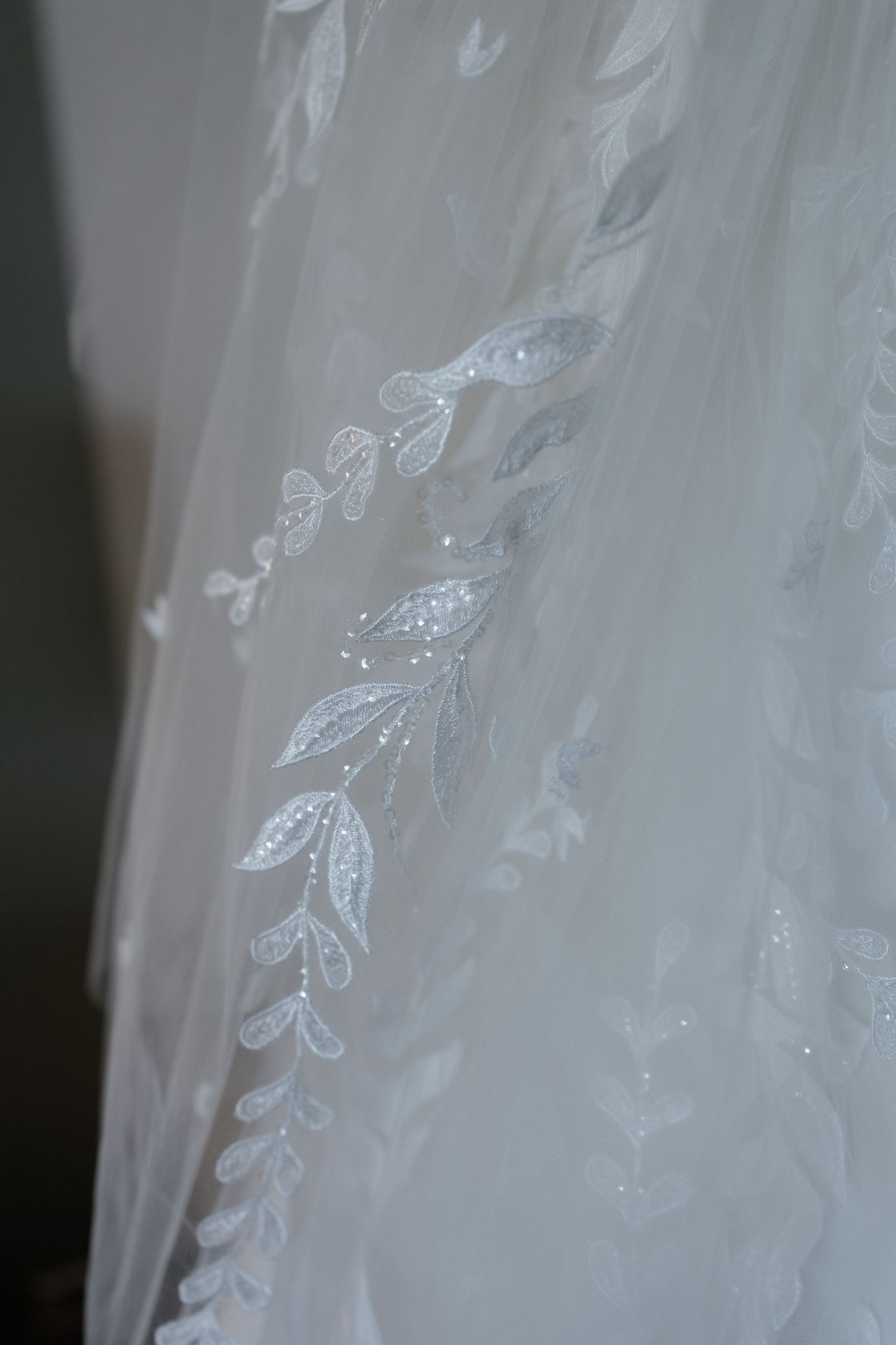 Delicate white lace and embroidered floral details on a wedding dress fabric.