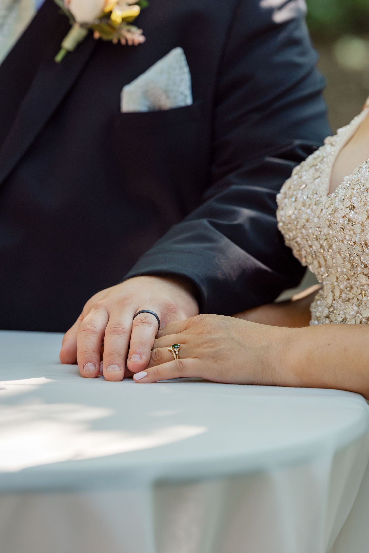 Close-up of bride and groom holding hands on a table, showing wedding rings.
