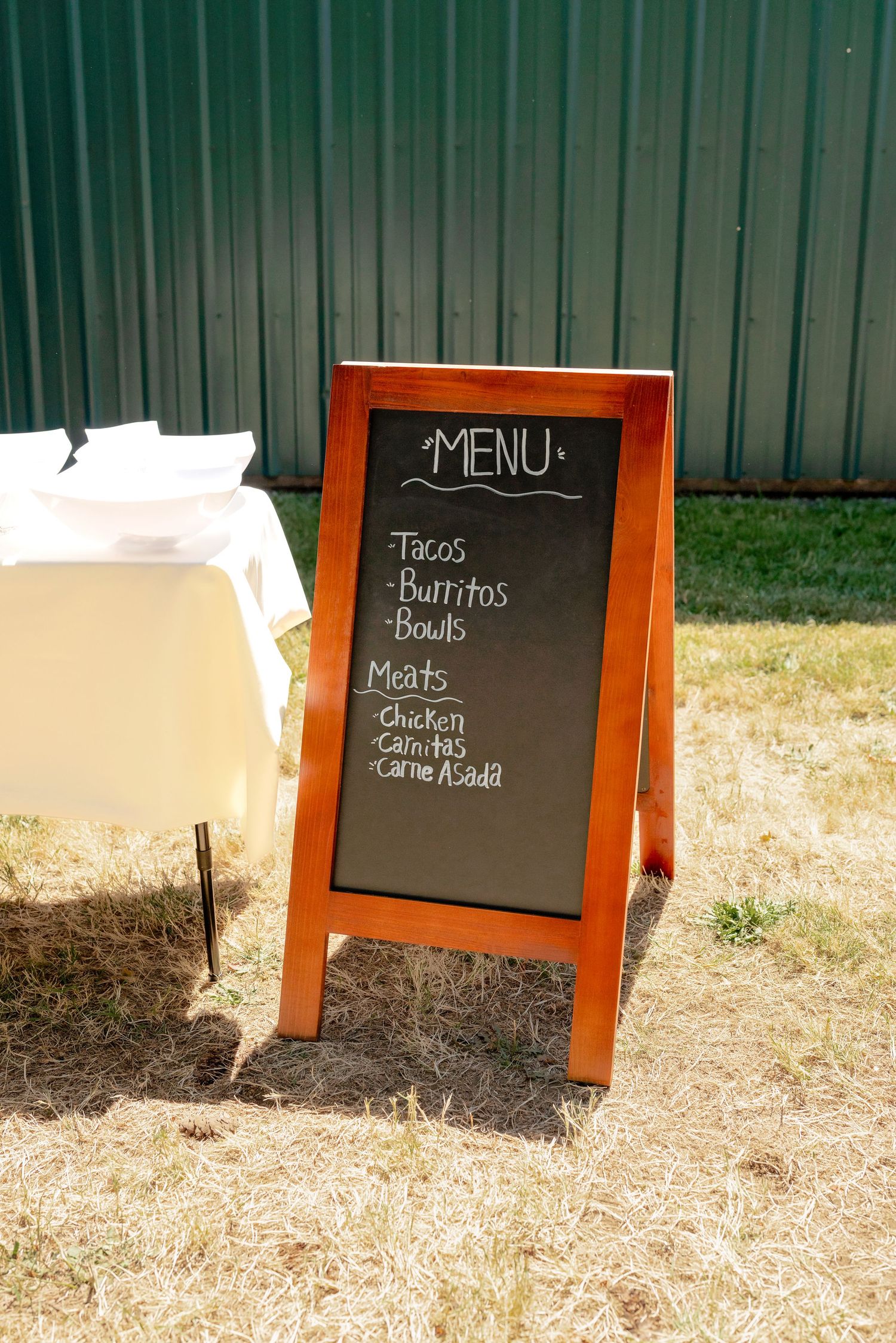 Outdoor chalkboard menu sign displaying tacos, burritos, bowls, chicken, carnitas, and carne asada at a wedding reception.