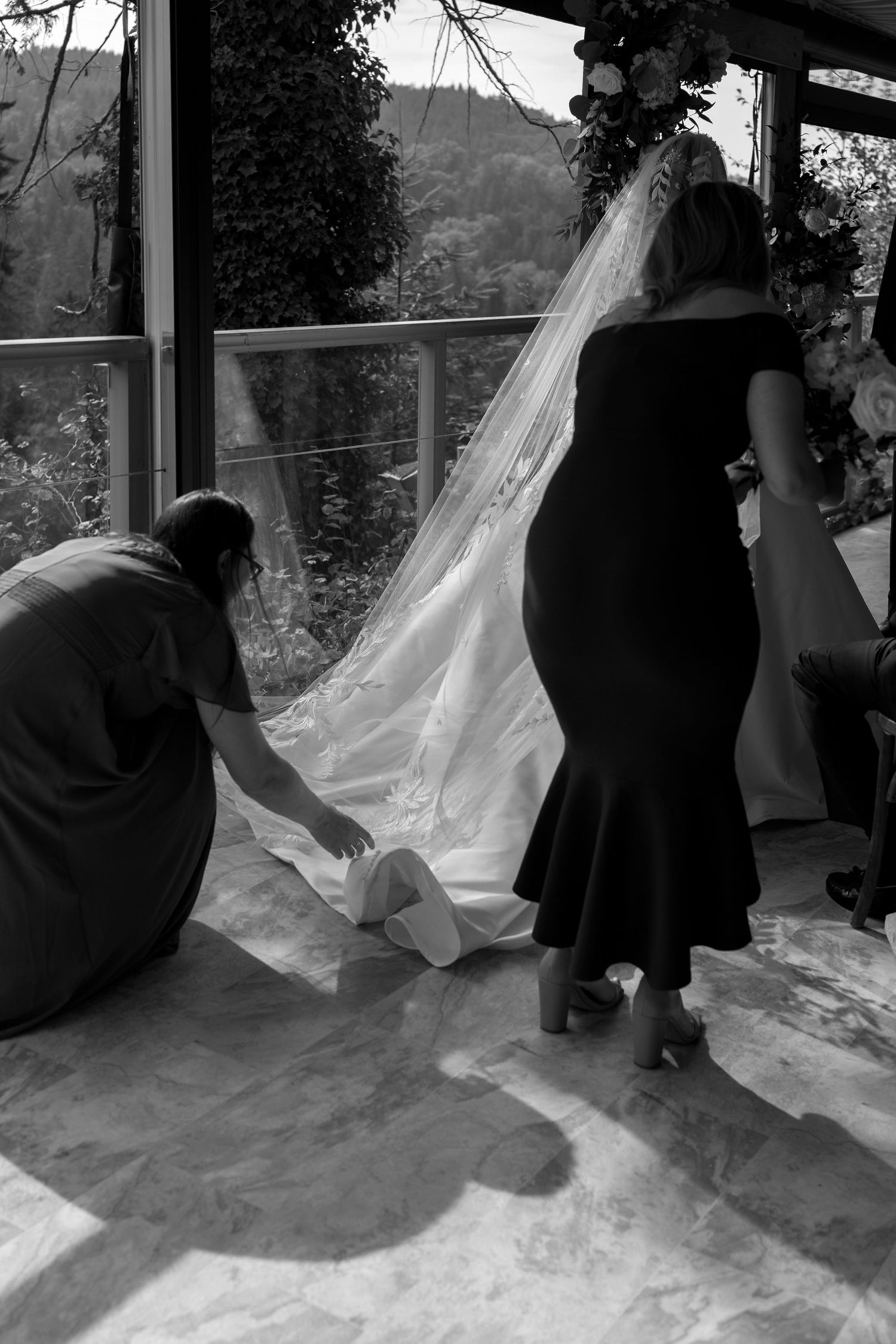 Black and white photo of flowing white fabric against a window with silhouettes in the background.