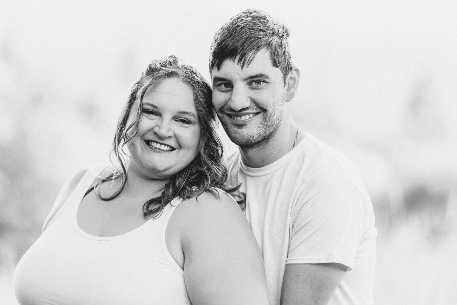 A black and white portrait of a happy couple smiling together outdoors.