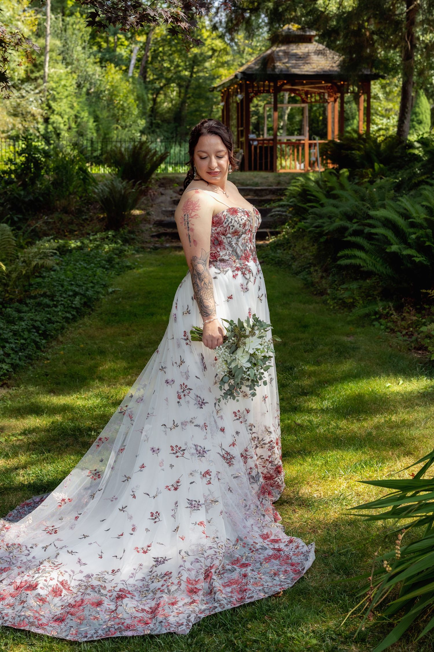 Bride in floral print wedding dress poses in garden setting.