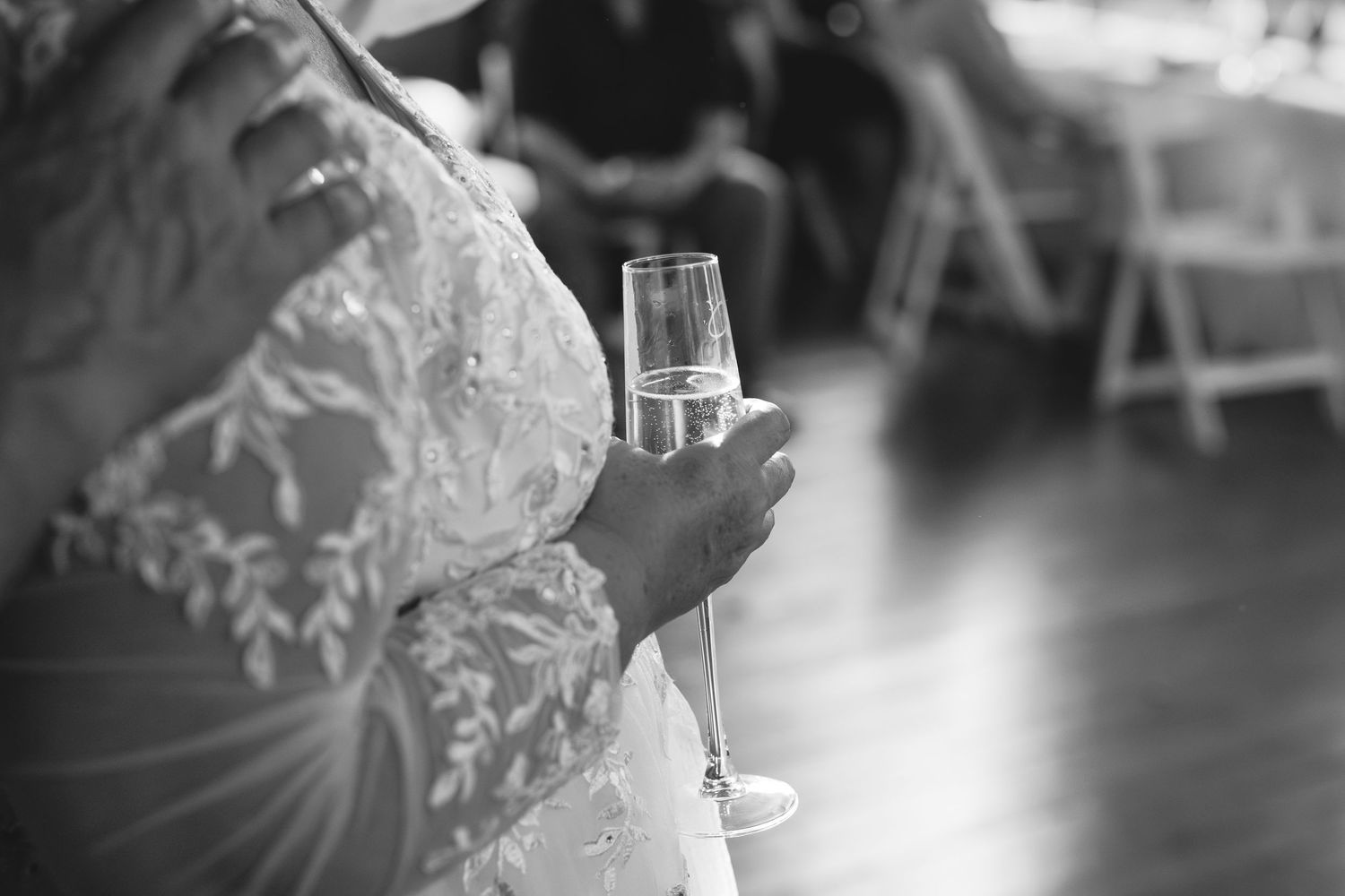 A delicate lace-detailed dress and champagne glass held in soft black and white focus.