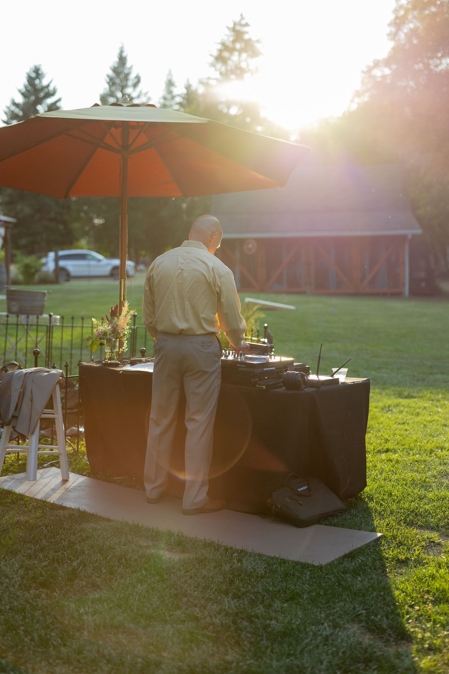 Outdoor catering setup with grills and orange umbrellas during sunset on a grassy lawn.