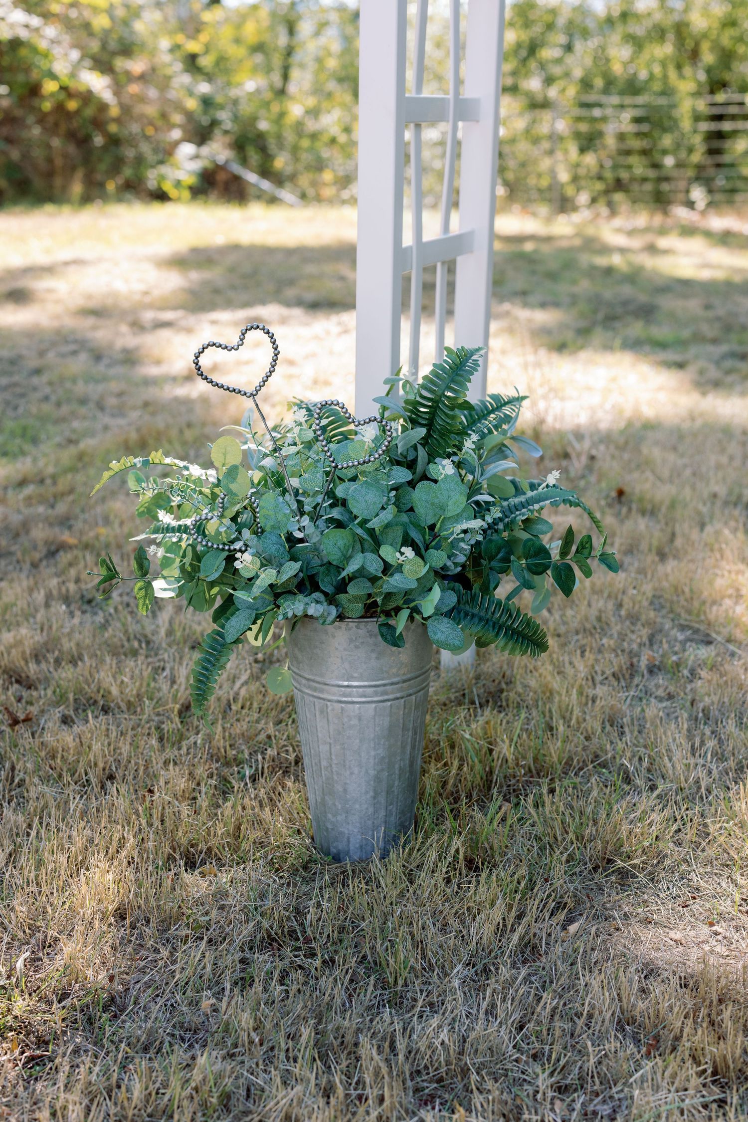 A rustic metal bucket filled with fresh greenery and ferns featuring a decorative heart accent.