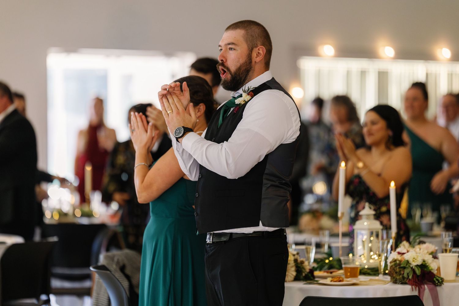 Wedding reception guests dancing and celebrating in an indoor venue with ambient lighting.