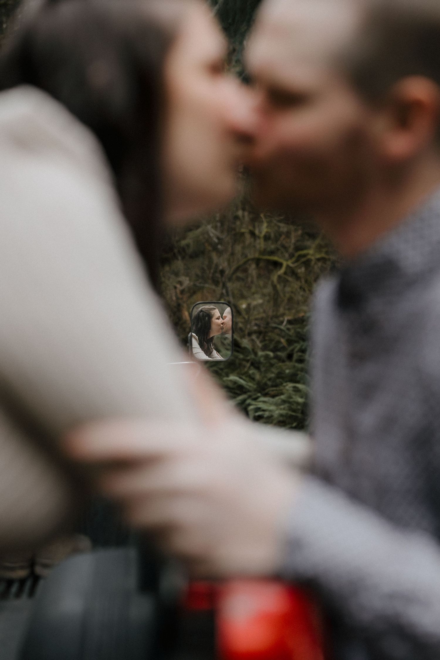 Blurred intimate moment captured outdoors with bokeh effect and greenery in background.