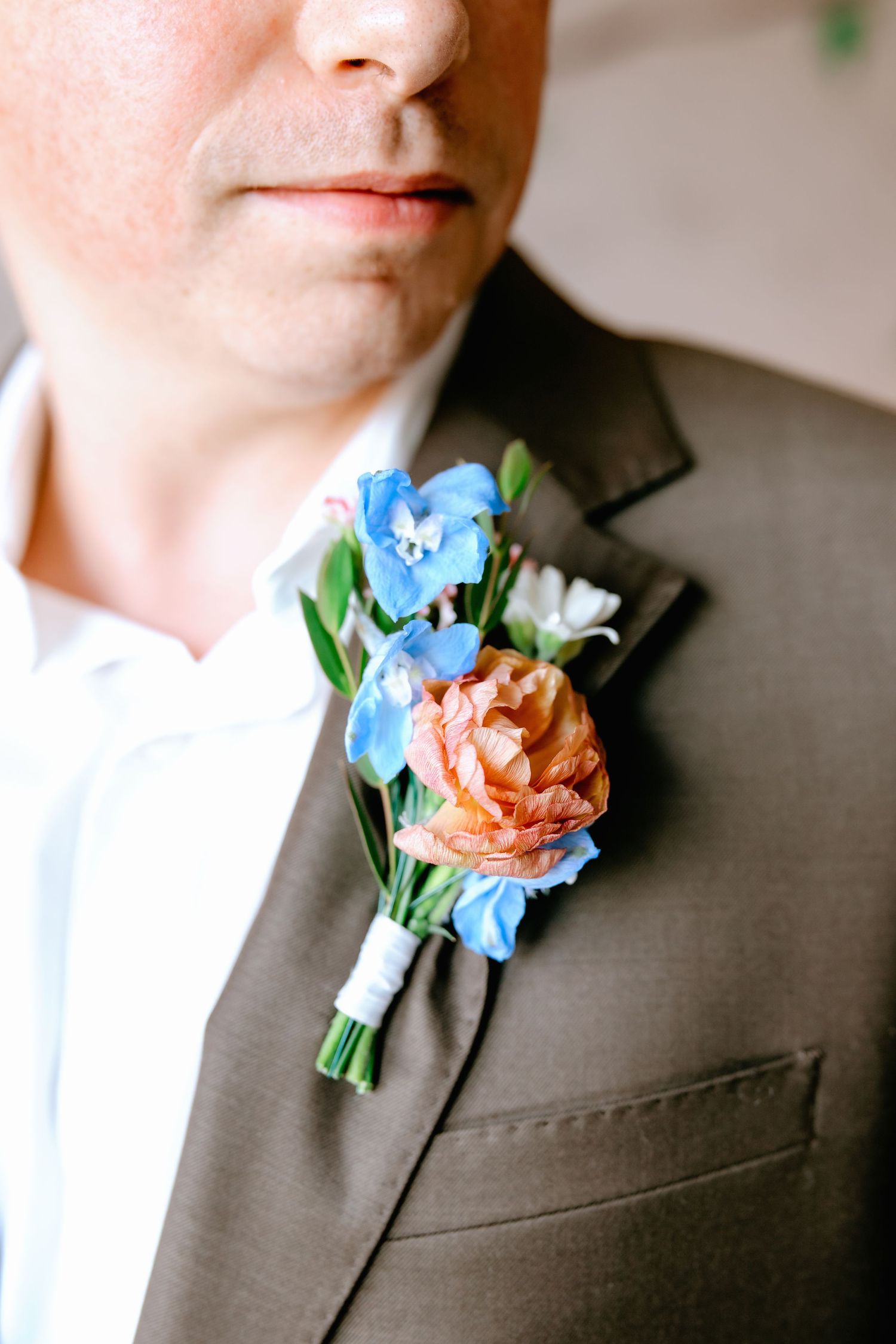 Groom wearing brown suit with colorful boutonniere featuring blue and peach flowers at wedding.