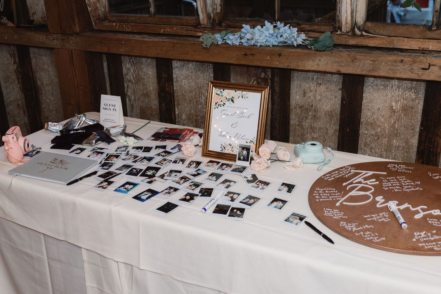 Wedding guest book table with Polaroid photos, wooden sign, and floral decor.