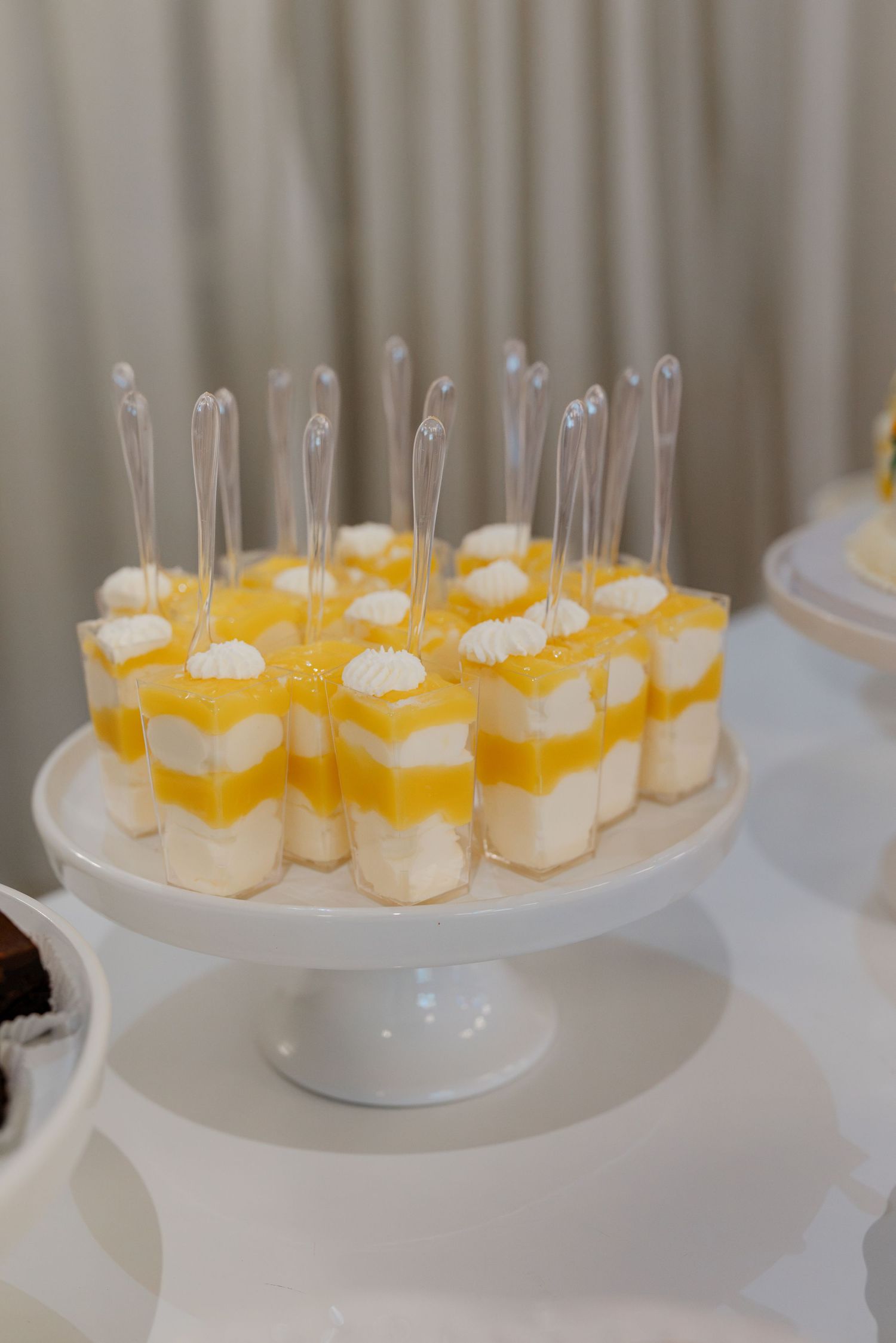 Elegant dessert display of layered mango and cream shooters with spoons on a white cake stand.